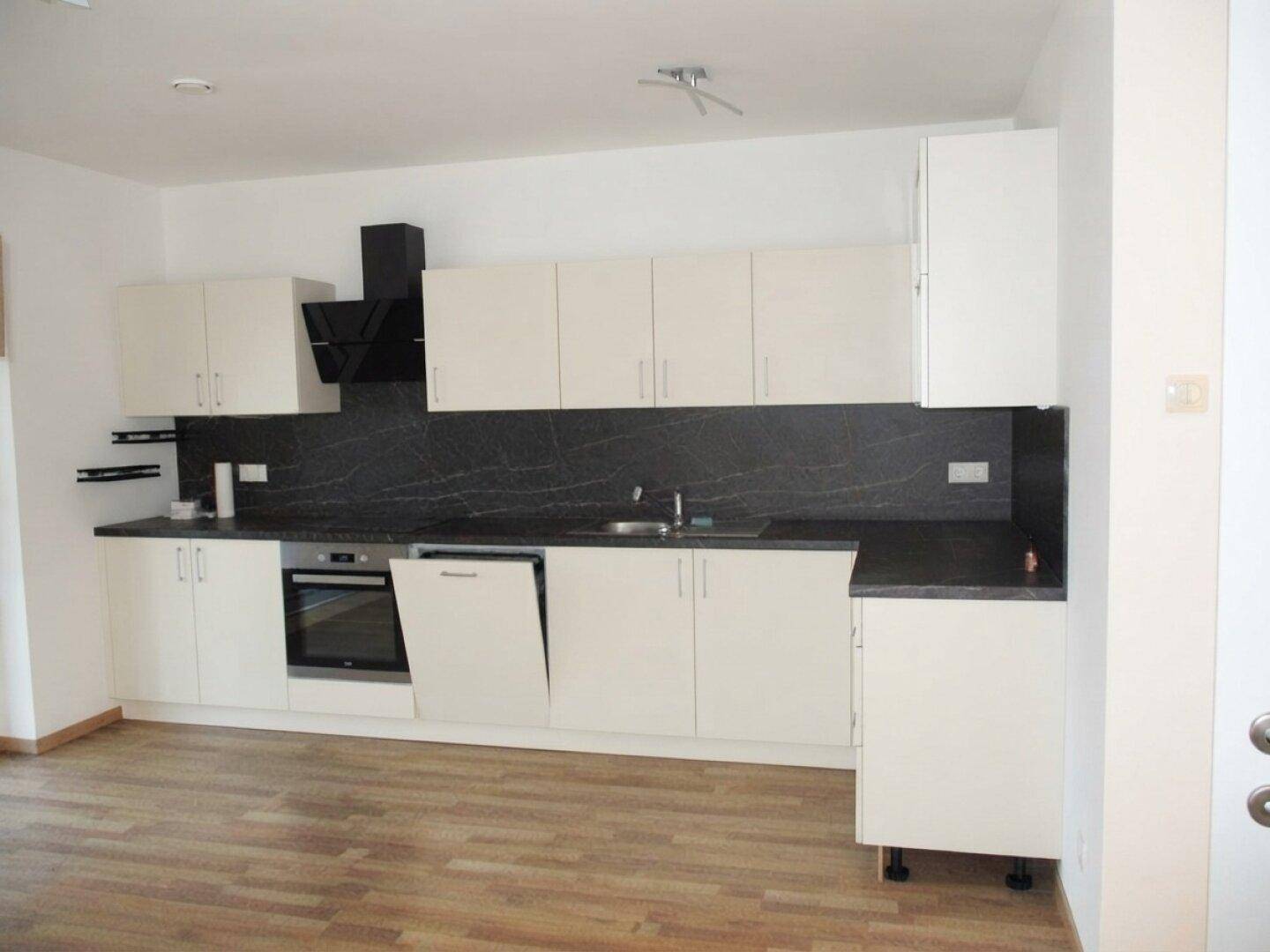 Helle Einbauküche mit weißen Schränken, dunkler Arbeitsplatte und integrierten Geräten in modernem Design.