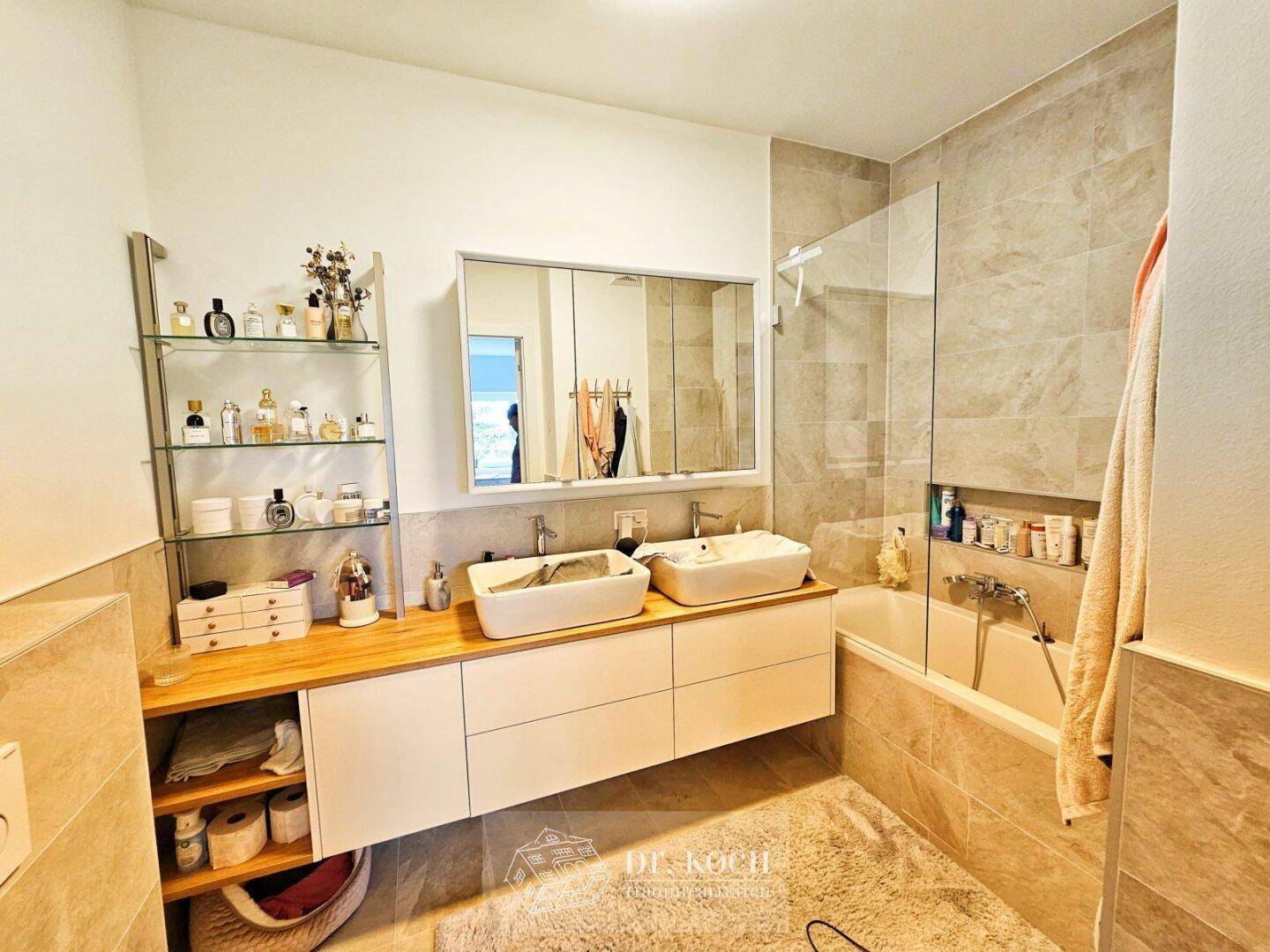 Modernes Badezimmer mit Doppelwaschbecken, Badewanne und Duschbereich, ausgestattet mit hellen Fliesen.