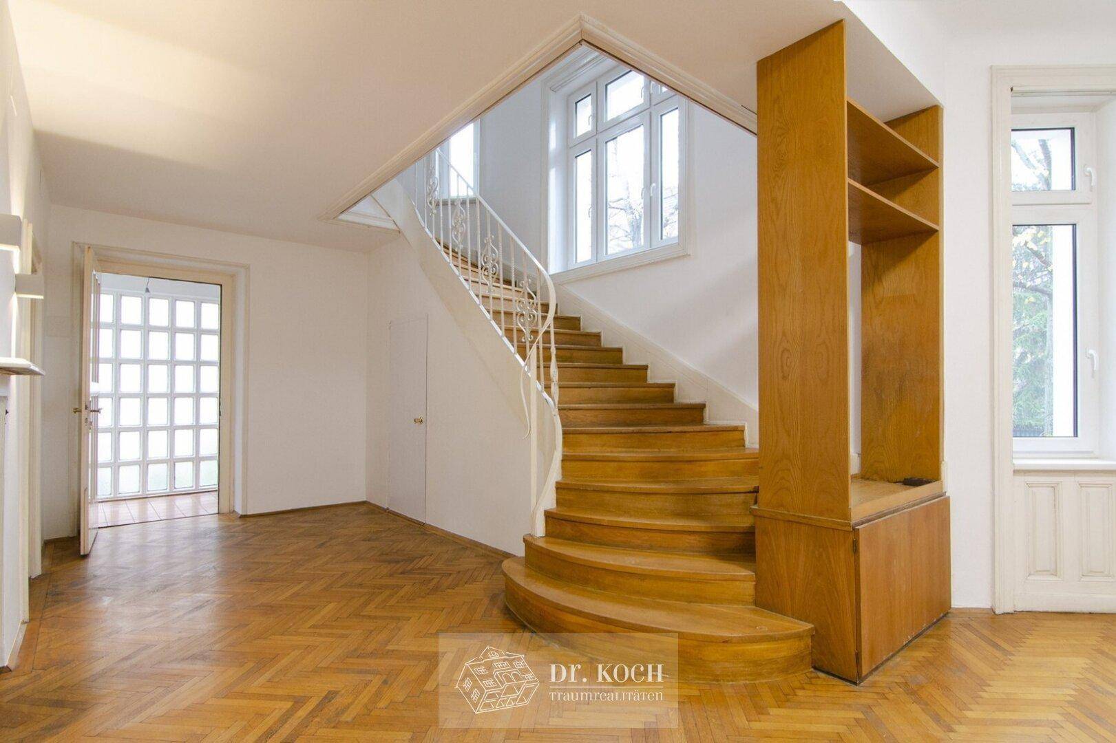 Geräumiger Eingangsbereich mit geschwungener Holztreppe und integriertem Regal.