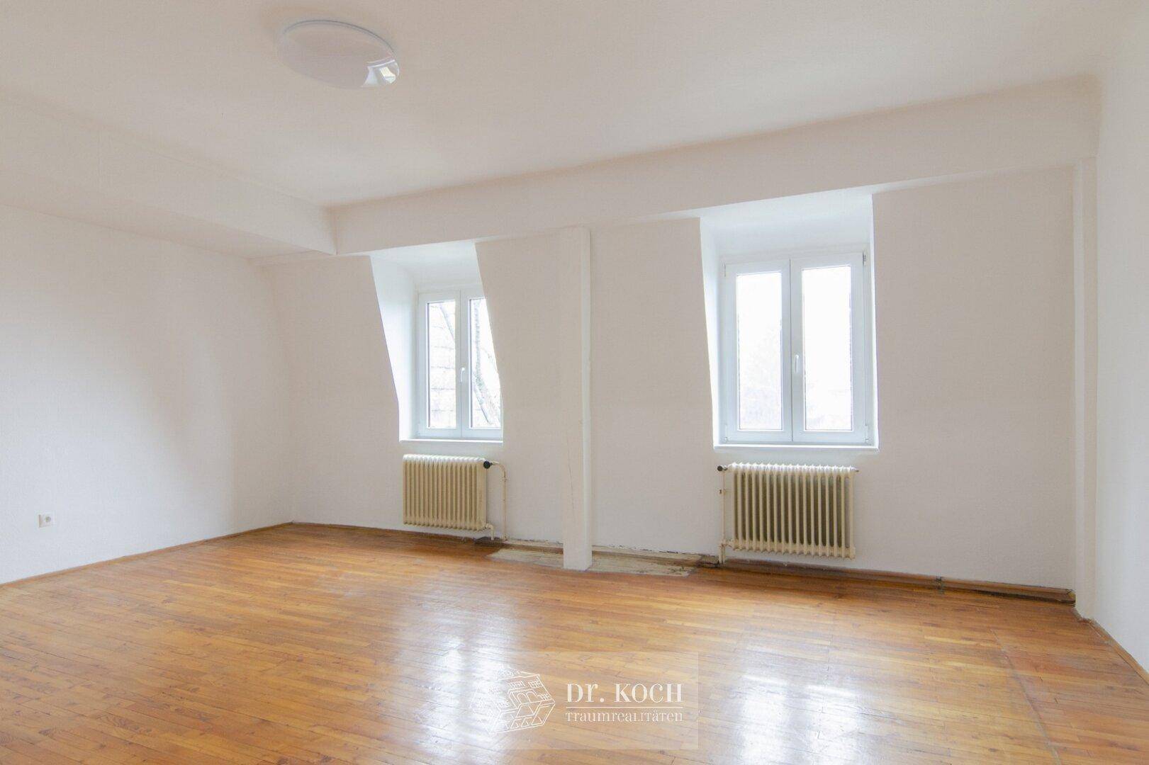 Helles Zimmer mit Holzboden und zwei Fenstern, ideal als Schlaf- oder Arbeitszimmer.