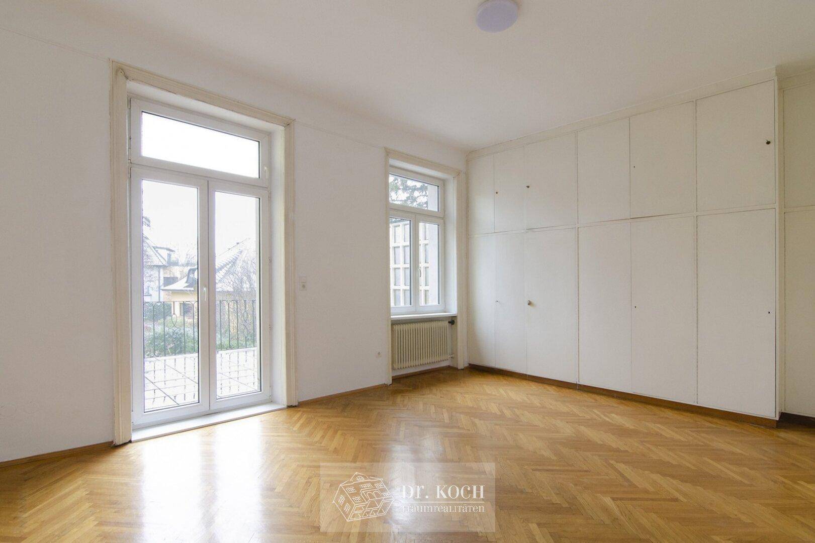 Geräumiges Schlafzimmer mit Einbauschränken, Holzboden und Zugang zum französischen Balkon.