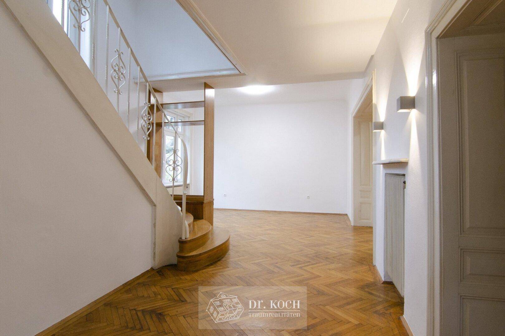 Heller Flur mit eleganter Holztreppe, Fischgrätparkett und Wandleuchten.
