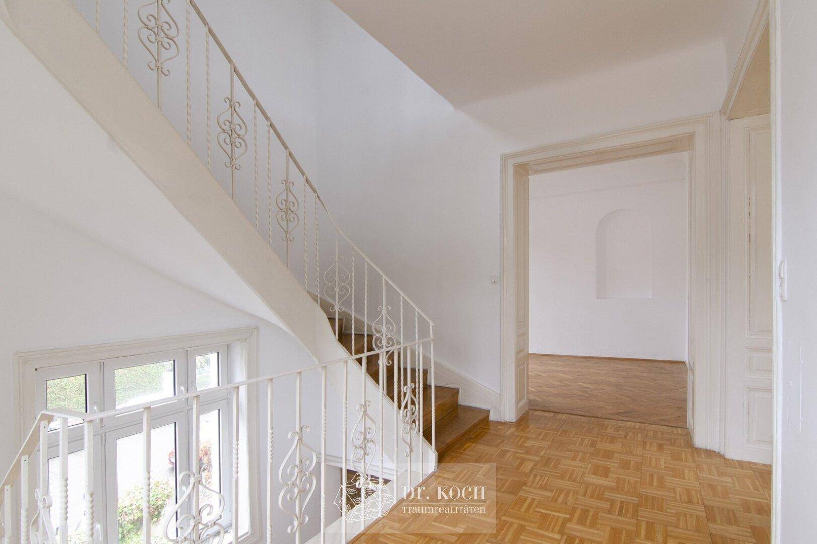 Treppenhaus mit geschwungenem Geländer und Blick in angrenzende Räume.