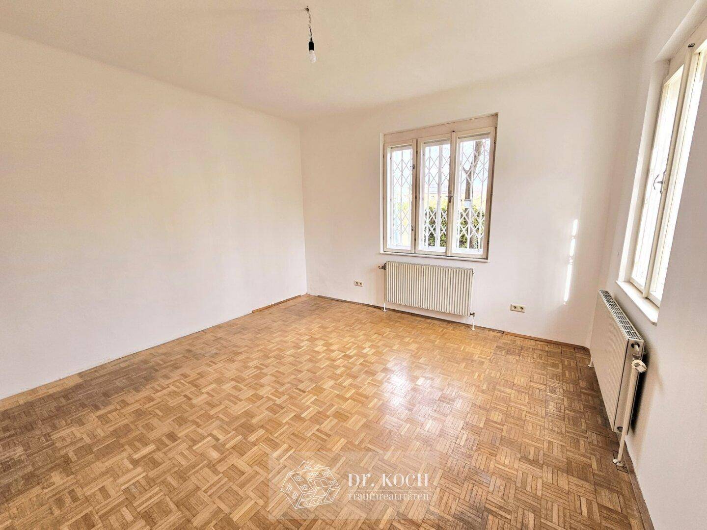 Helles Zimmer mit Parkettboden und Fenster mit dekorativem Gitter.