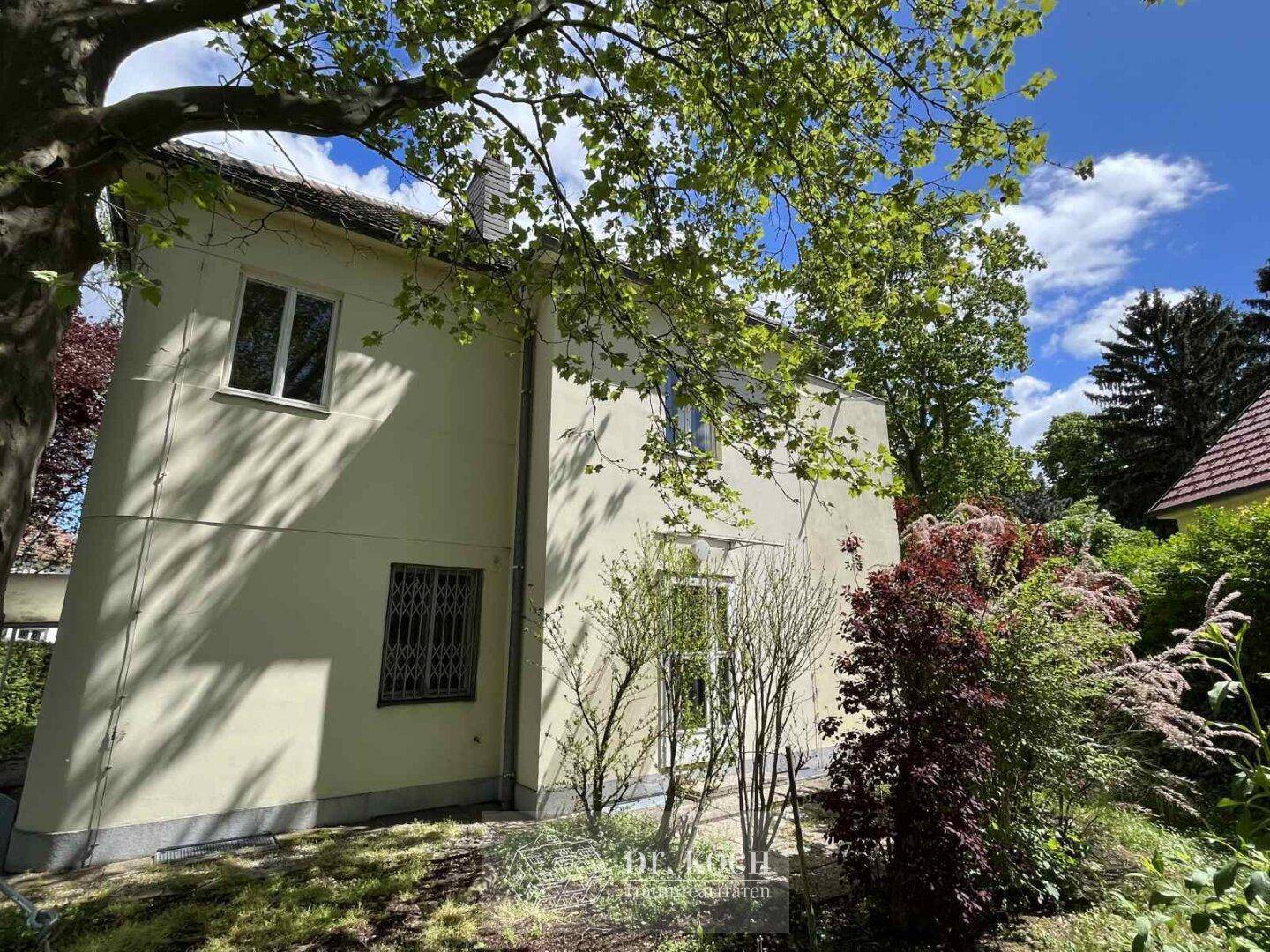 Seitenansicht des Hauses mit Gartenbereich und üppiger Vegetation unter blauem Himmel.