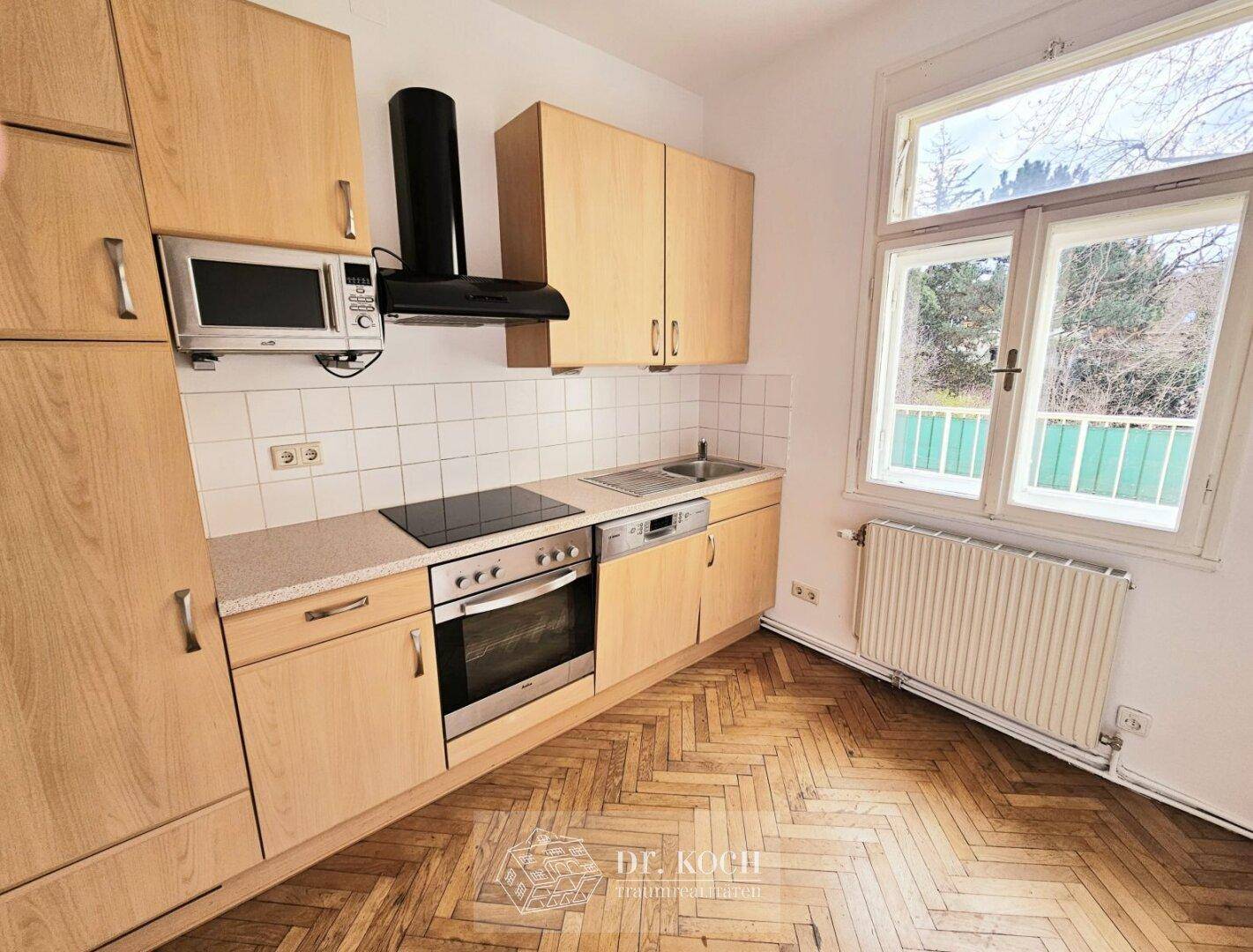 Funktionale Küche mit Holzschränken, Einbaugeräten und Blick ins Grüne.