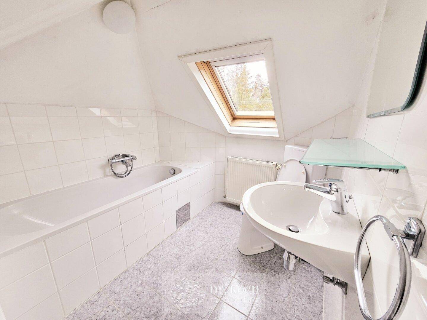 Modernes Badezimmer im Dachgeschoss mit Badewanne, Waschbecken und Dachfenster.