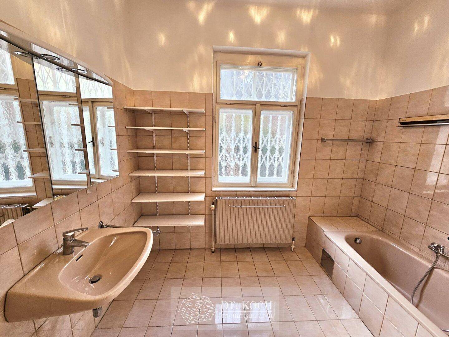 Badezimmer mit beigefarbenen Fliesen, Badewanne und Fenster für natürliche Belüftung.
