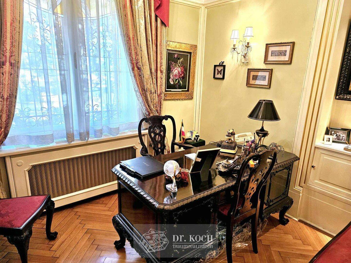 Klassisches Arbeitszimmer mit Holzparkett, großem Schreibtisch und Fenster mit Blick ins Grüne.