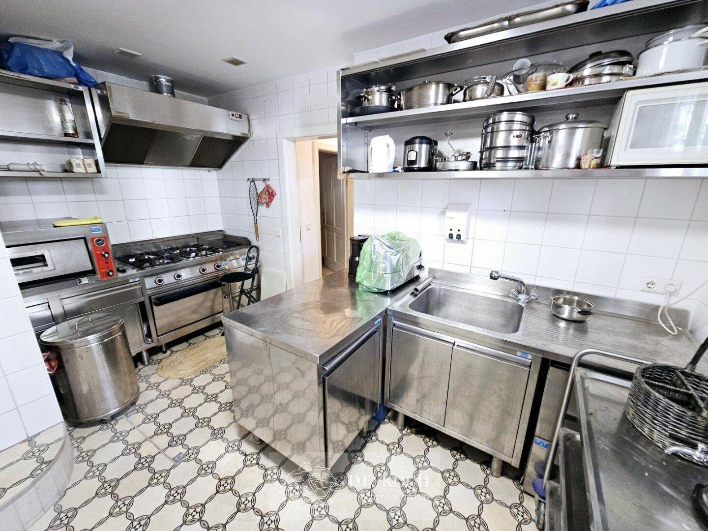 Funktionale Industrieküche mit Edelstahlgeräten, Gasherd und Fliesenboden für professionelles Kochen.