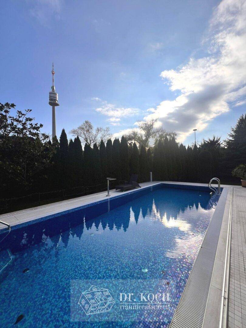 Außenpool mit blauen Mosaikfliesen und Blick auf den Donauturm in der Ferne.