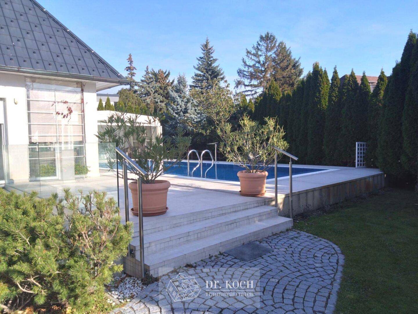 Außenbereich mit Pool, Steintreppe und gepflegter Gartenanlage neben dem Haus.