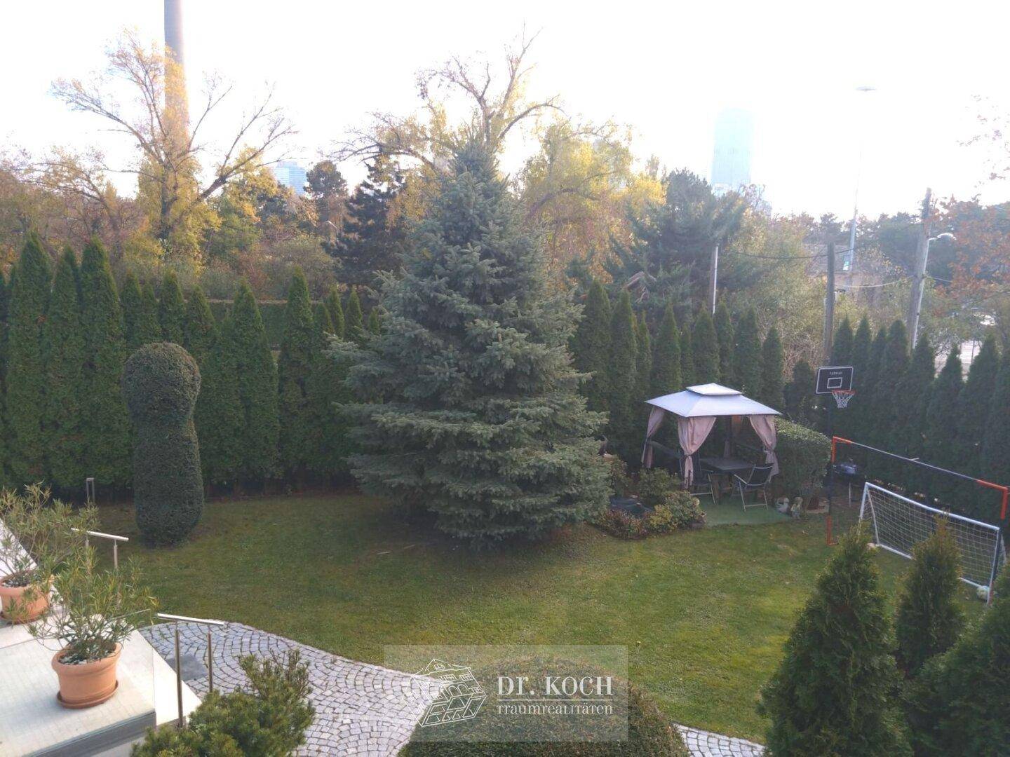 Weitläufiger Garten mit Rasenfläche, Bäumen, Pavillon und Sportmöglichkeiten.