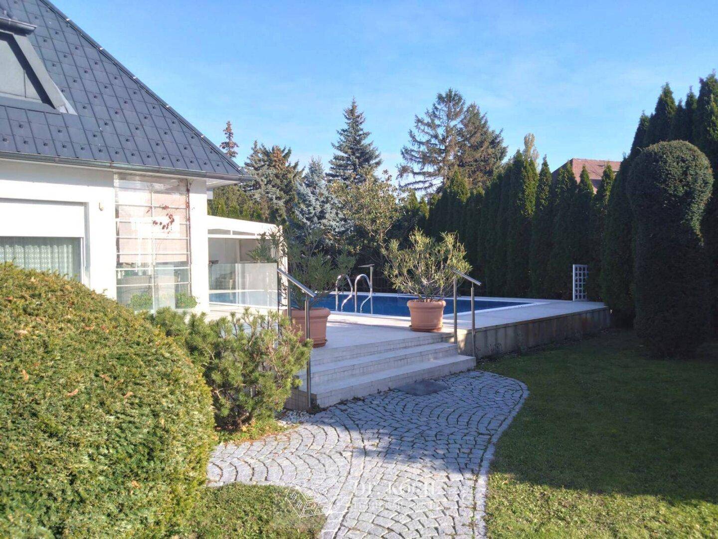 Hausansicht mit Garten, Steintreppe und dem Poolbereich im Hintergrund.