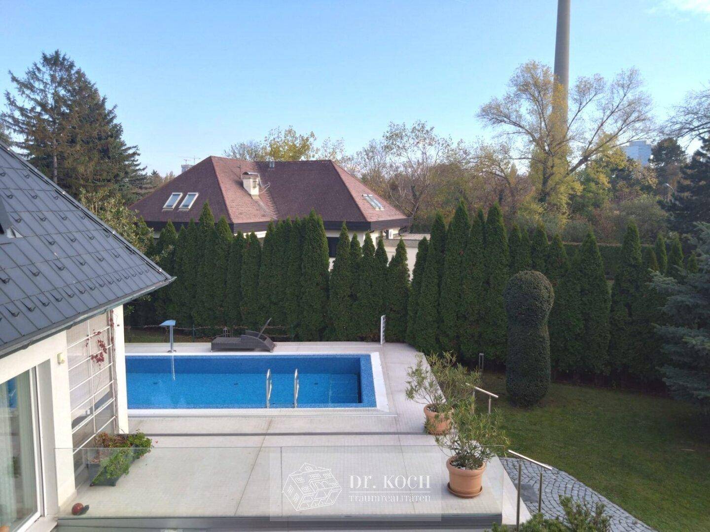 Überblick über den Poolbereich und den weitläufigen Garten mit angrenzenden Häusern.