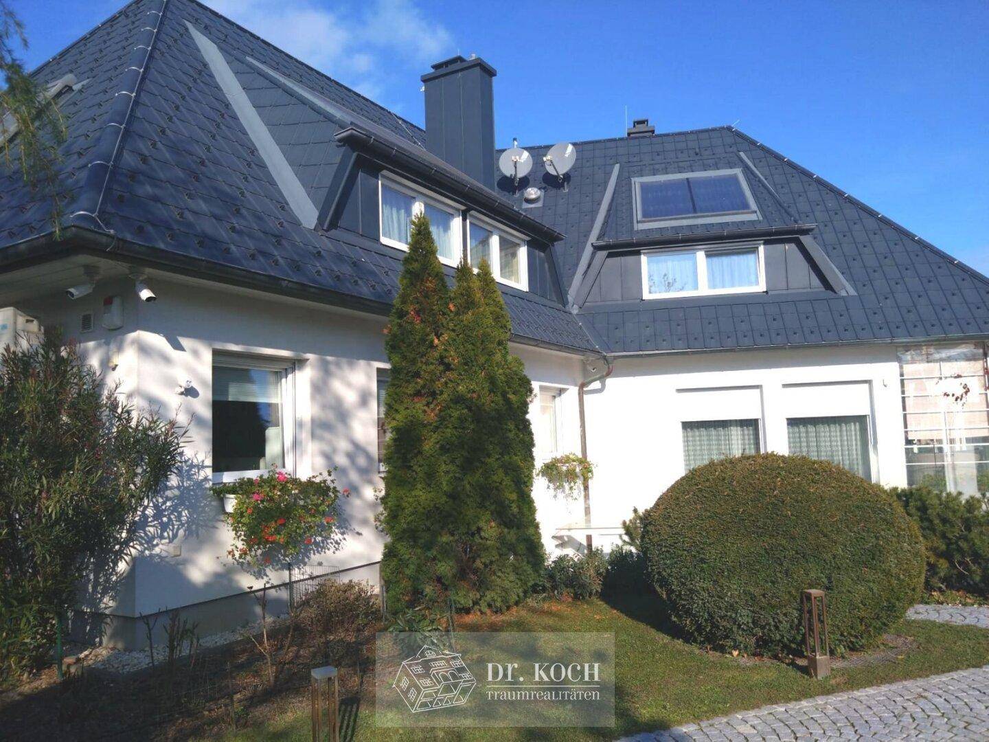 Detailansicht der Hausfassade mit Dachgauben und gepflegter Gartenbepflanzung.