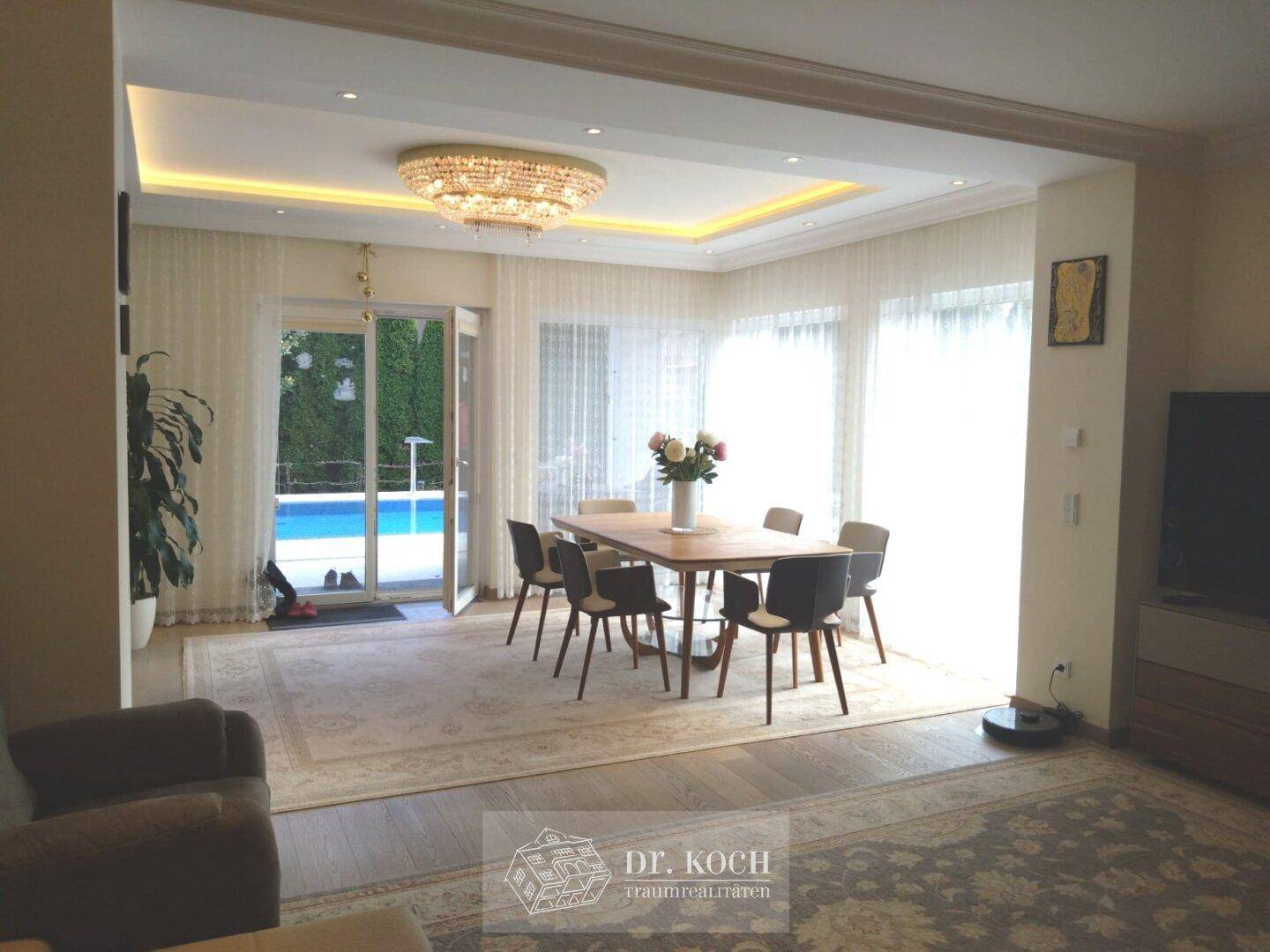 Eleganter Essbereich mit großem Holztisch, Kronleuchter und Blick auf den Pool.