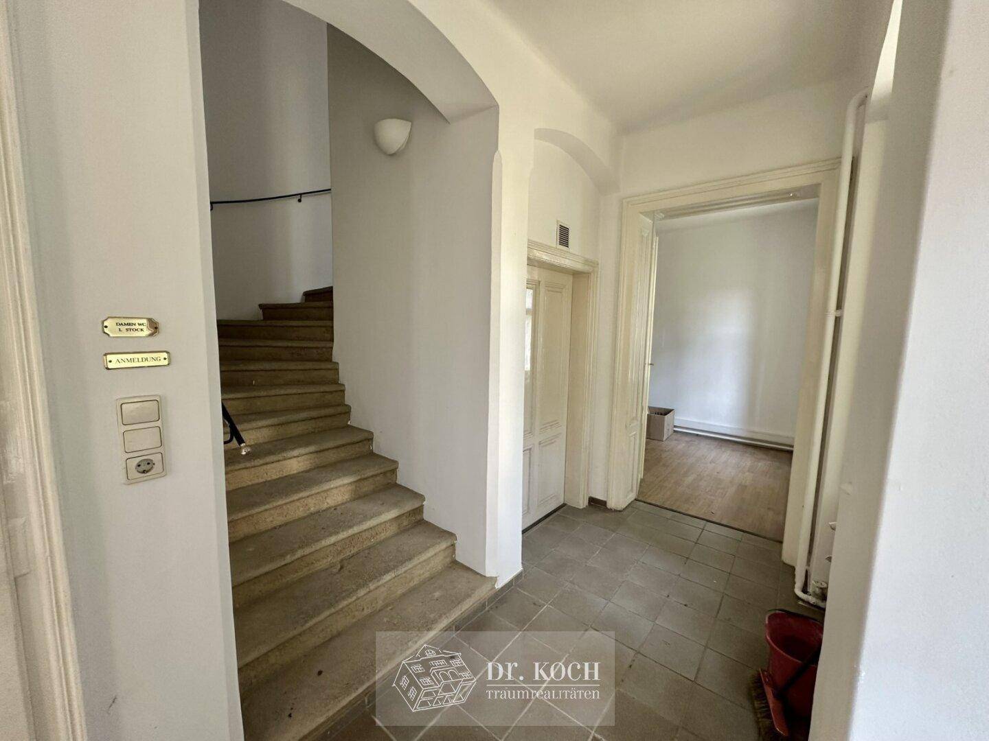 Heller Eingangsbereich mit Steinfliesenboden und einer geschwungenen Treppe zum Obergeschoss.