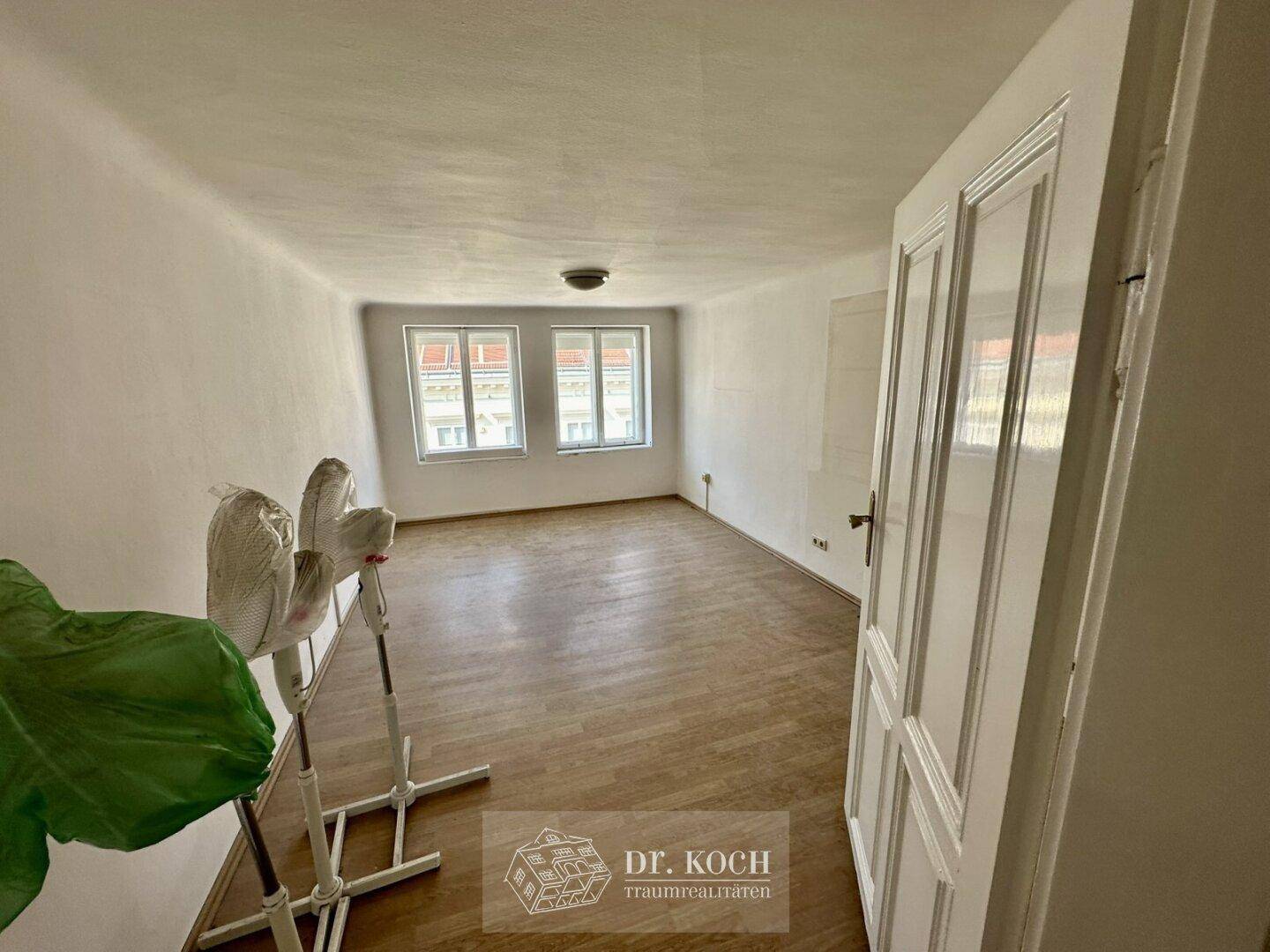 Helles Schlafzimmer mit Holzboden und zwei Fenstern, bereit zur Renovierung.