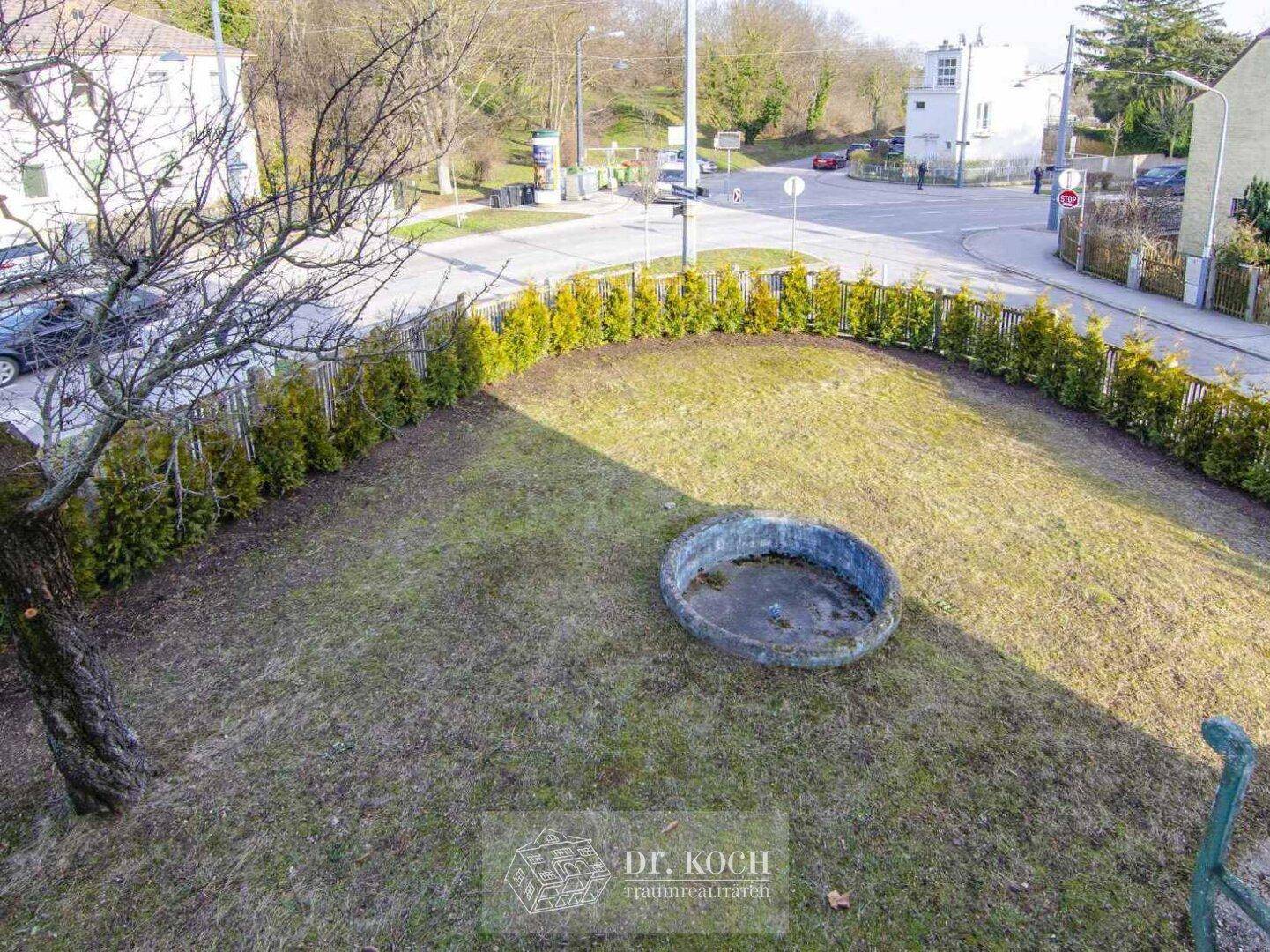 Gartenbereich mit Rasen, Hecke und Blick auf die umliegende Straße.