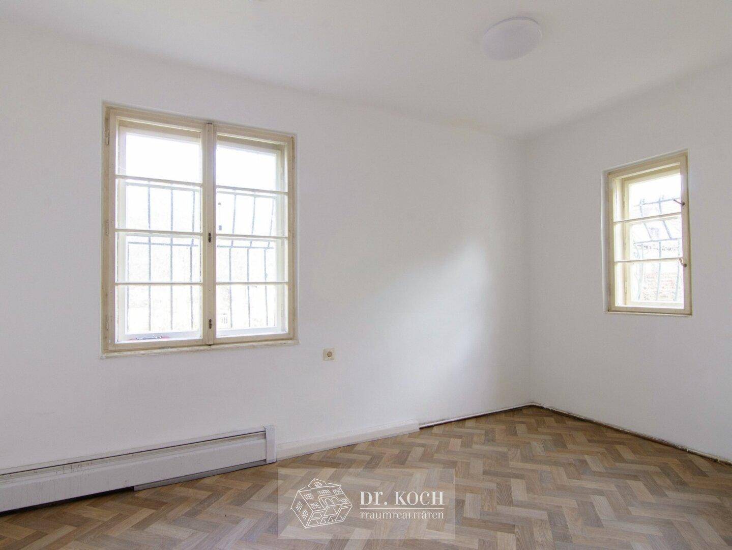 Lichtdurchfluteter Raum mit Parkettboden und zwei Fenstern, ideal für Schlaf- oder Arbeitszimmer.
