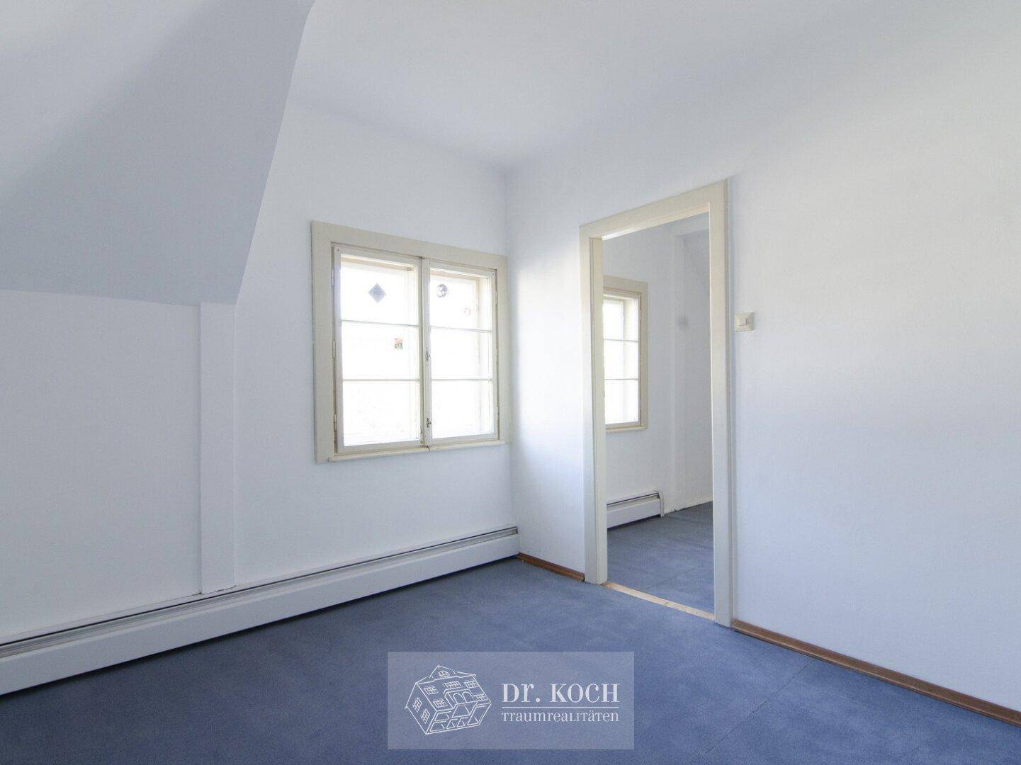 Dachgeschosszimmer mit blauem Teppichboden und natürlichem Lichteinfall durch das Fenster.