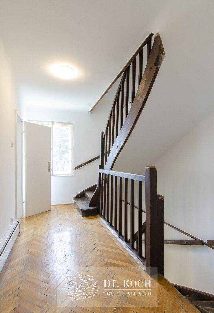 Geräumiger Flur mit Holztreppe und Fischgrätparkett, der die Etagen verbindet.