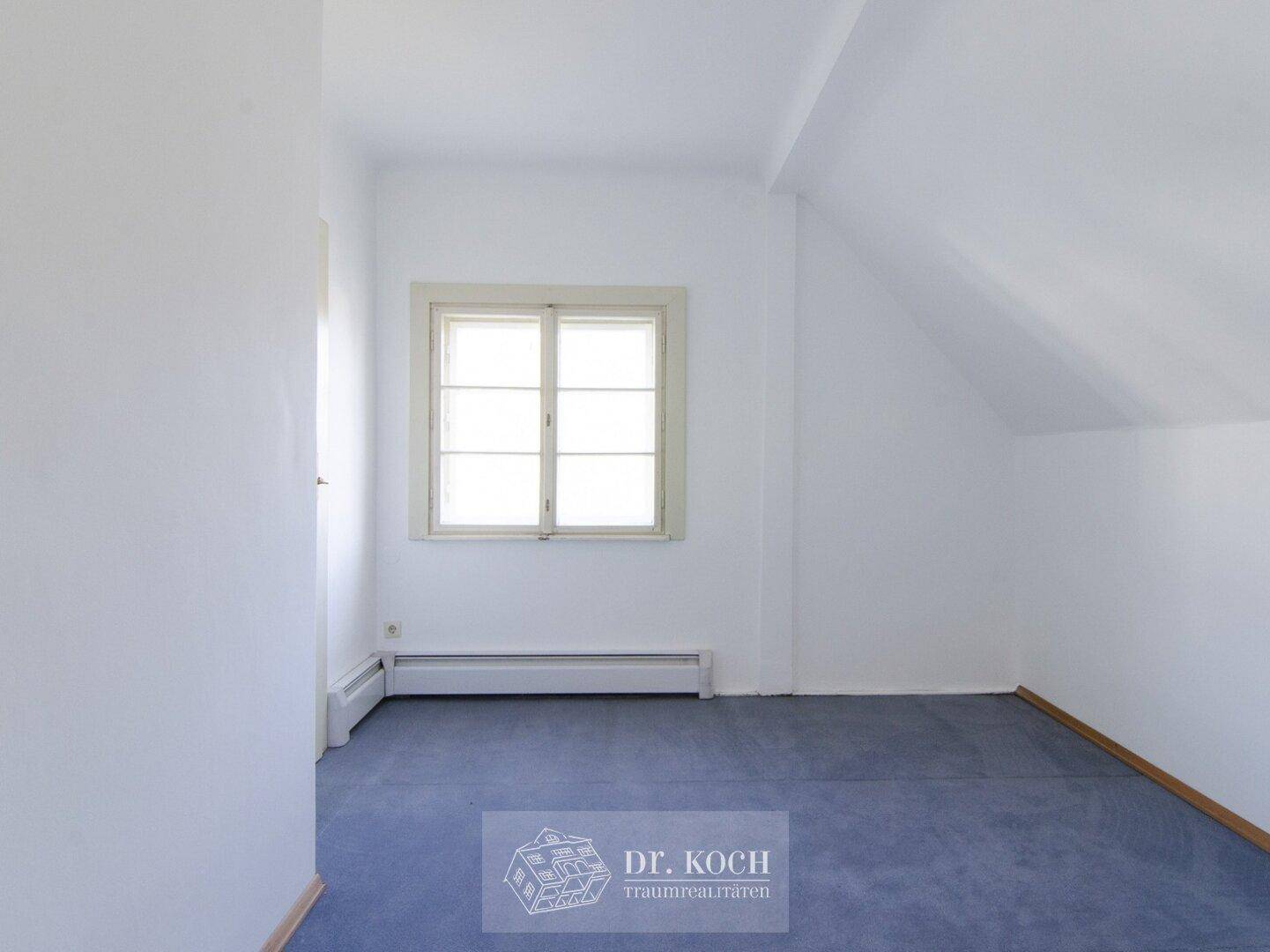 Dachgeschosszimmer mit blauem Teppichboden und Fenster, ideal als Kinder- oder Gästezimmer.