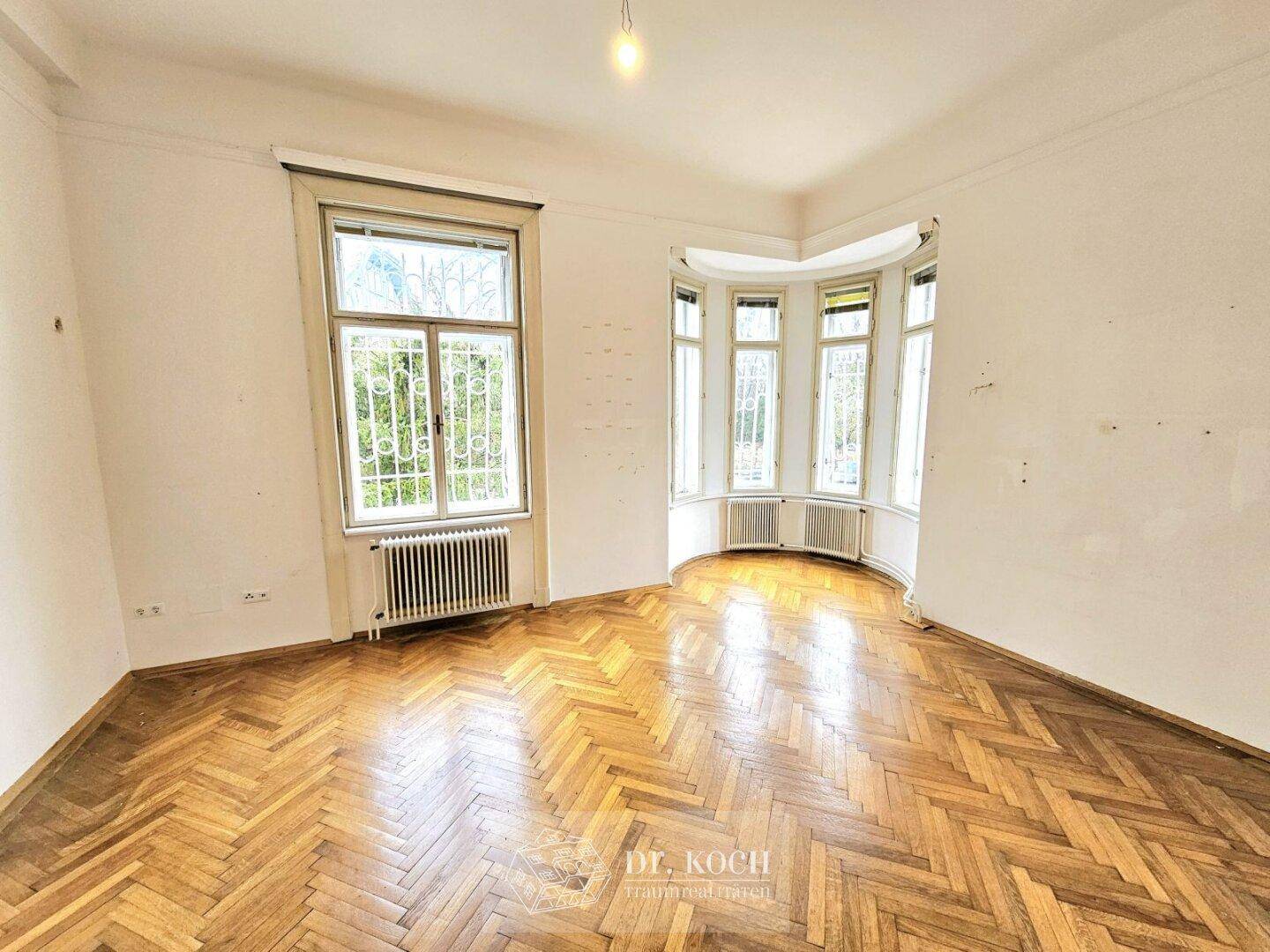 Helles Zimmer mit Erkerfenstern und Fischgrätparkett, ideal für ein Wohn- oder Schlafzimmer.