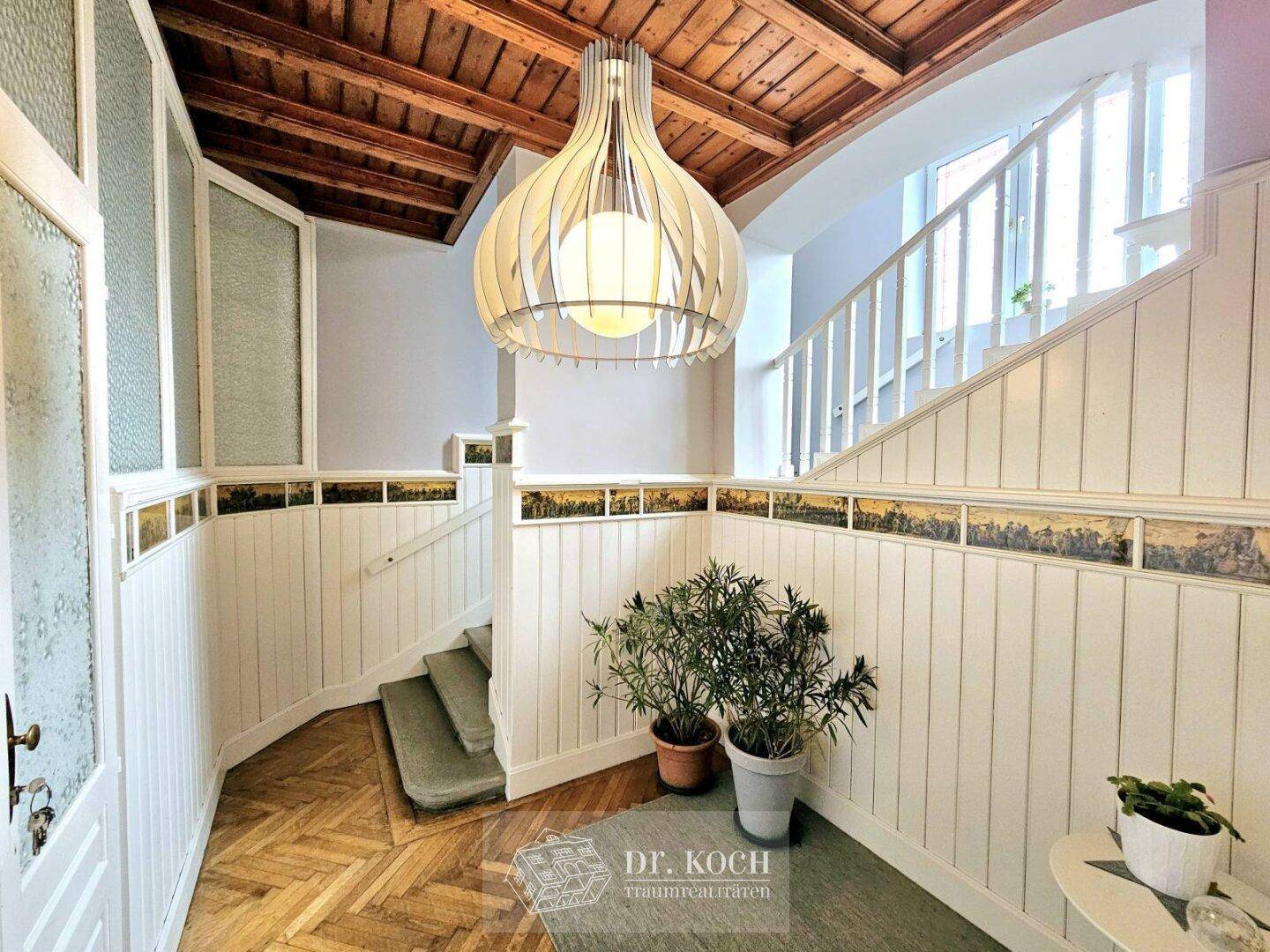 Heller Eingangsbereich mit Holzvertäfelung, Fischgrätparkett und einer eleganten Holztreppe.