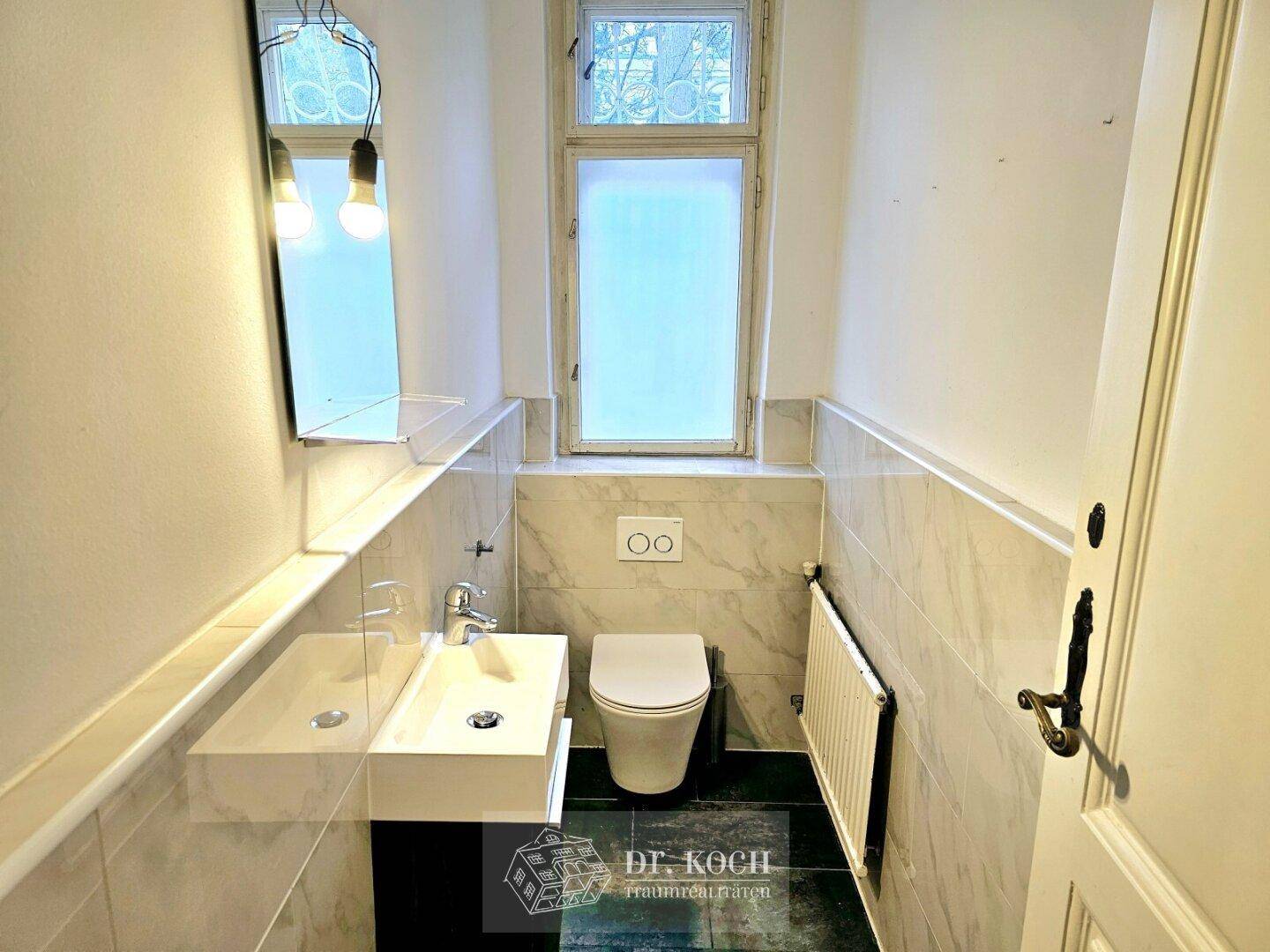 Modernes Gäste-WC mit Wand-WC, stilvollem Waschbecken und Fenster für Tageslicht.