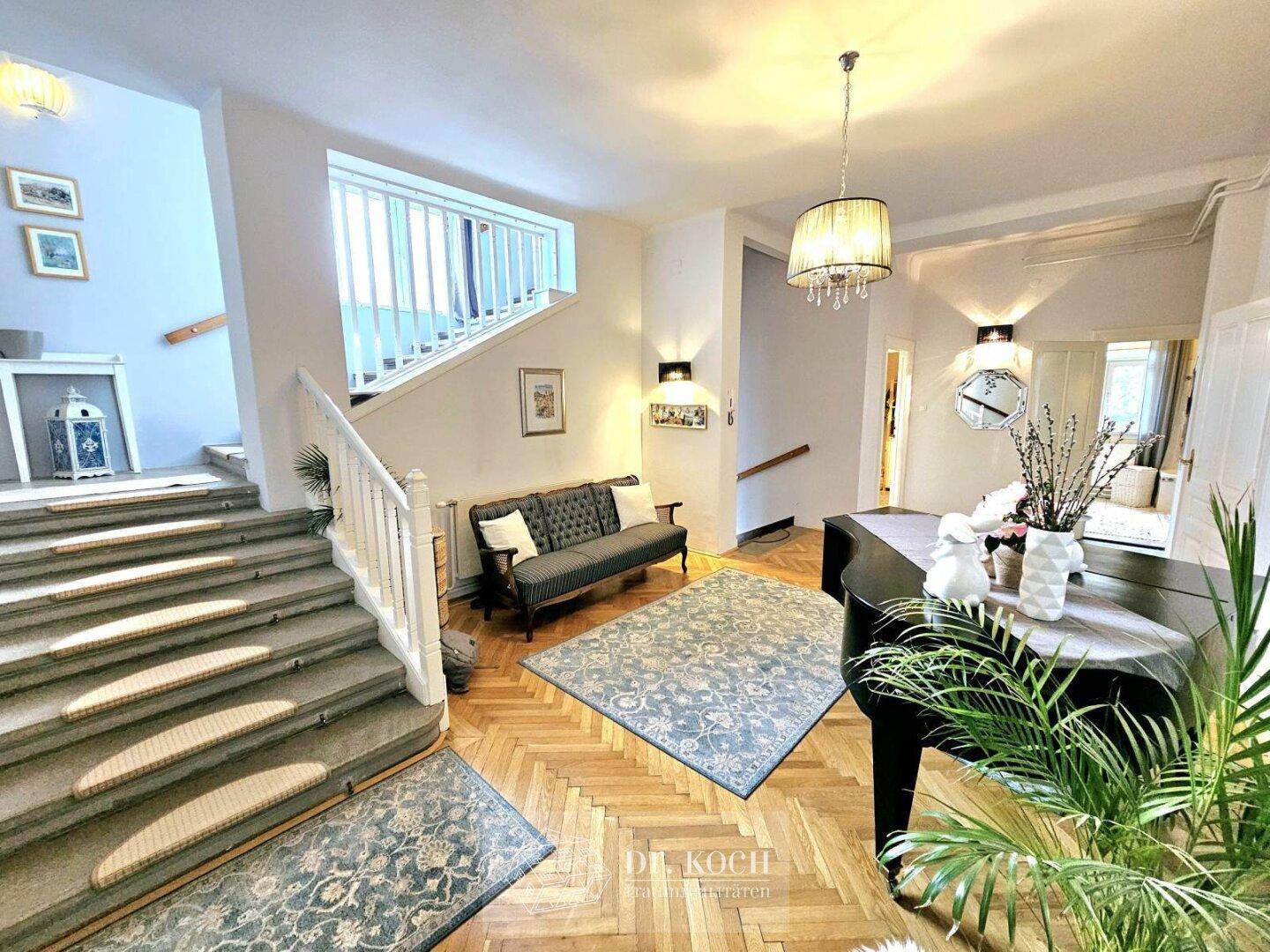 Großzügige Eingangshalle mit imposanter Treppe, Fischgrätparkett und einem Flügel.