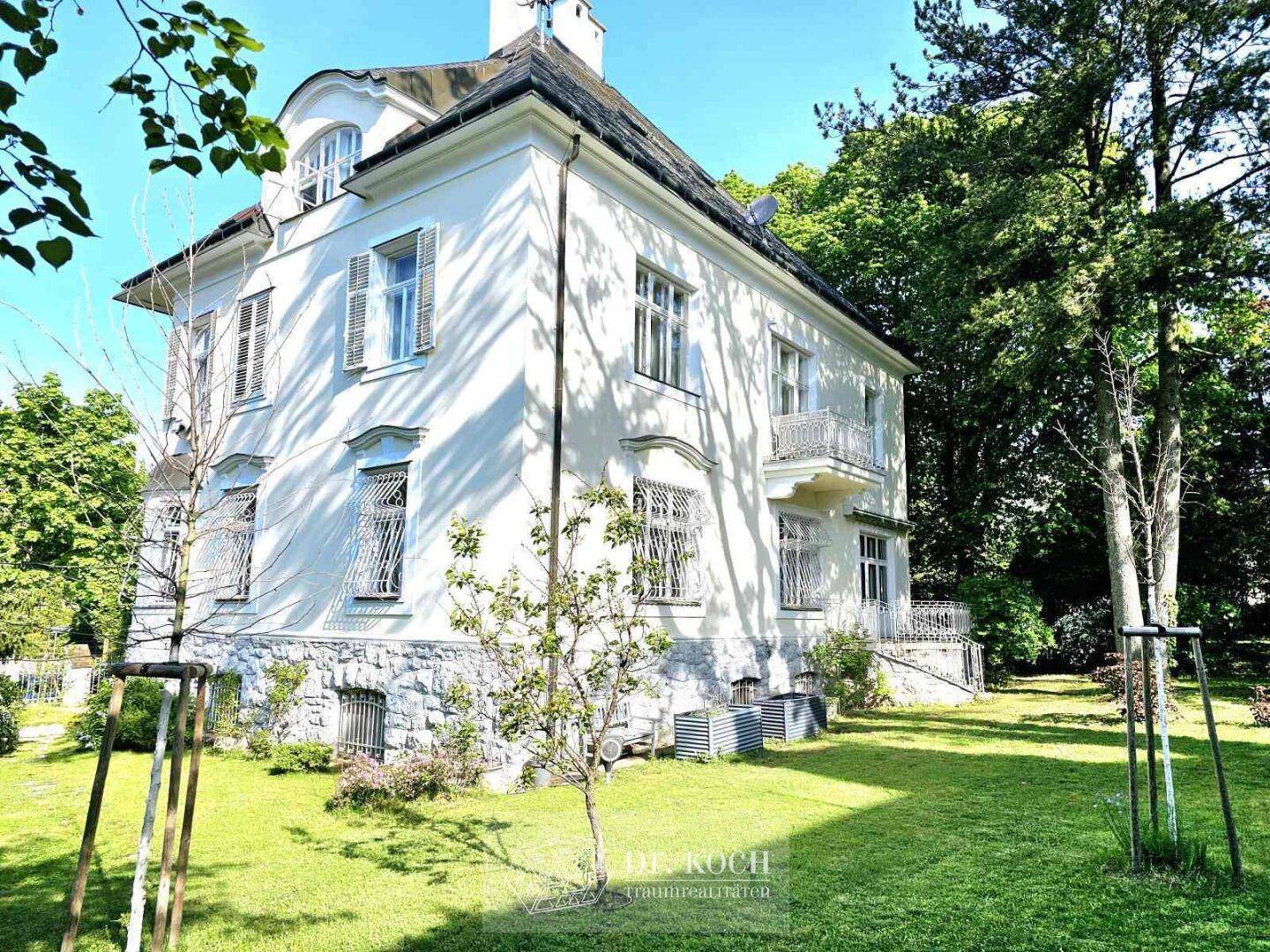 Seitlicher Blick auf die Villa mit großem, gepflegtem Garten und altem Baumbestand.