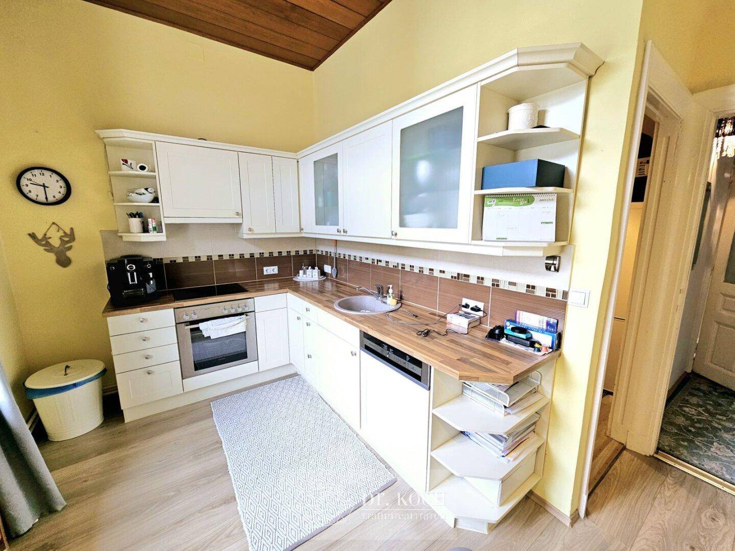 Funktionale Küche mit weißen Schränken, Holzarbeitsplatten und einer Holzdecke.