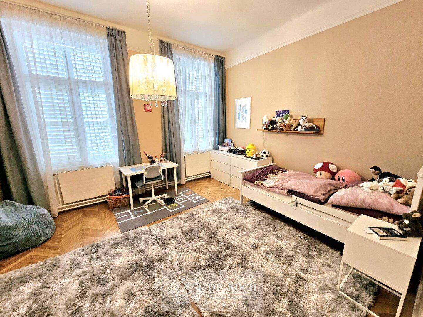 Helles Kinderzimmer mit Parkettboden, großem Fenster und einem Schreibtischbereich.