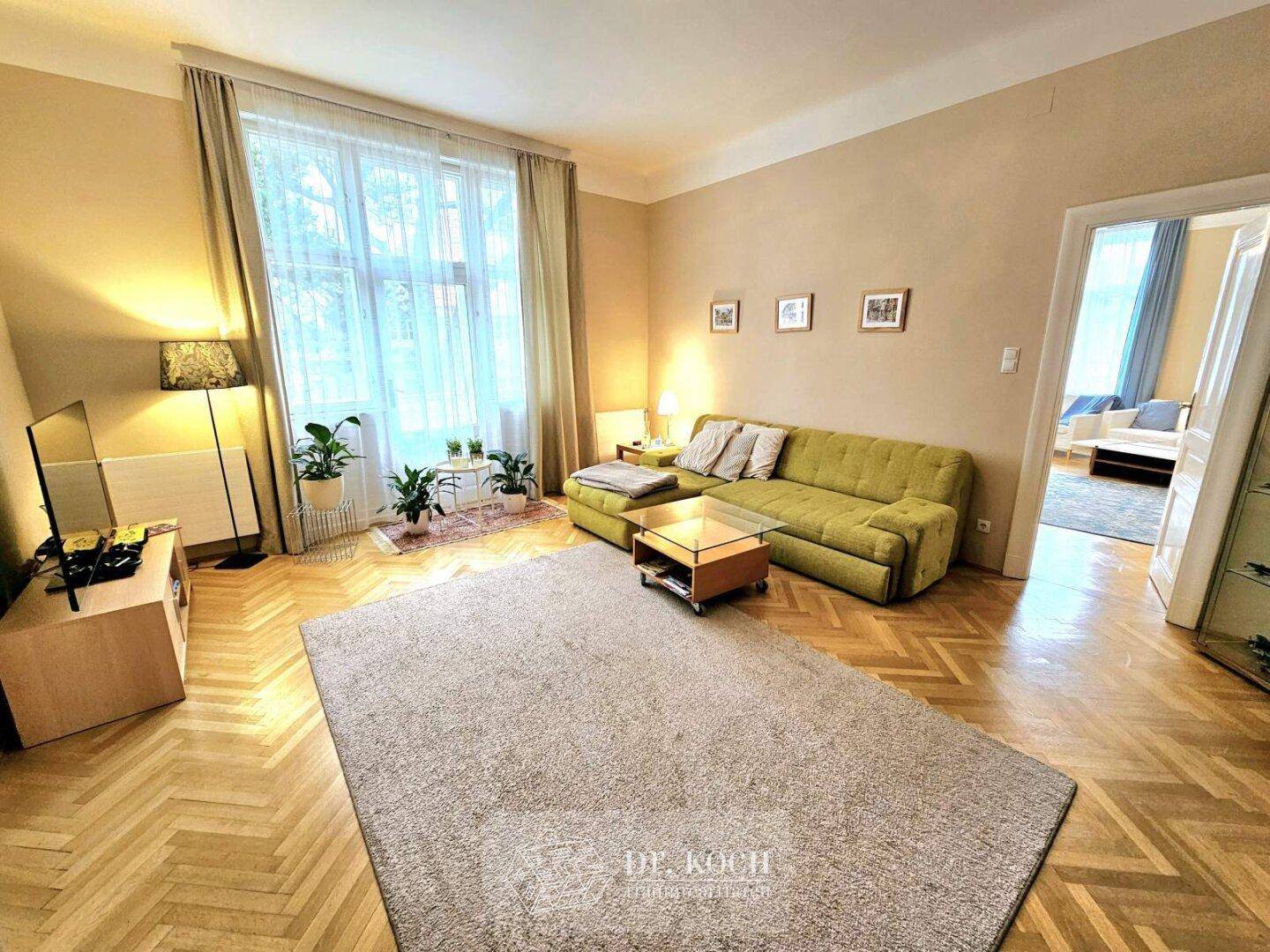 Gemütliches Wohnzimmer mit Parkettboden, großem Fenster und einem bequemen grünen Sofa.