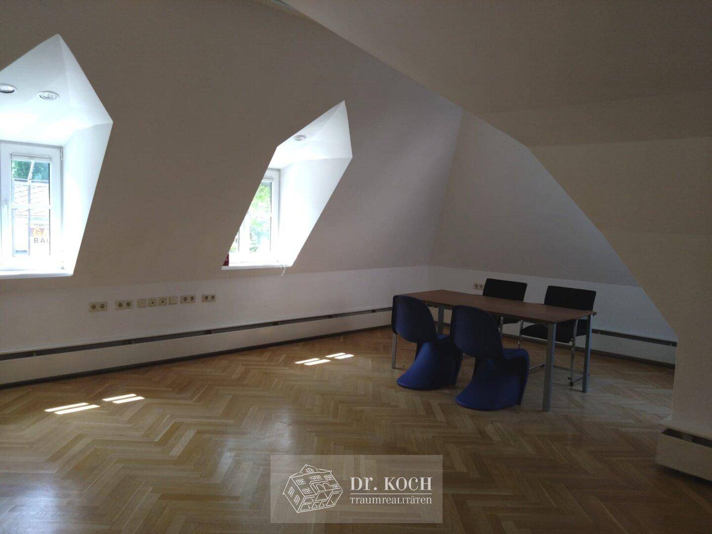 Helles Dachgeschossbüro mit schrägen Wänden, Holzboden und einem kleinen Besprechungstisch, ideal für kleine Teams.