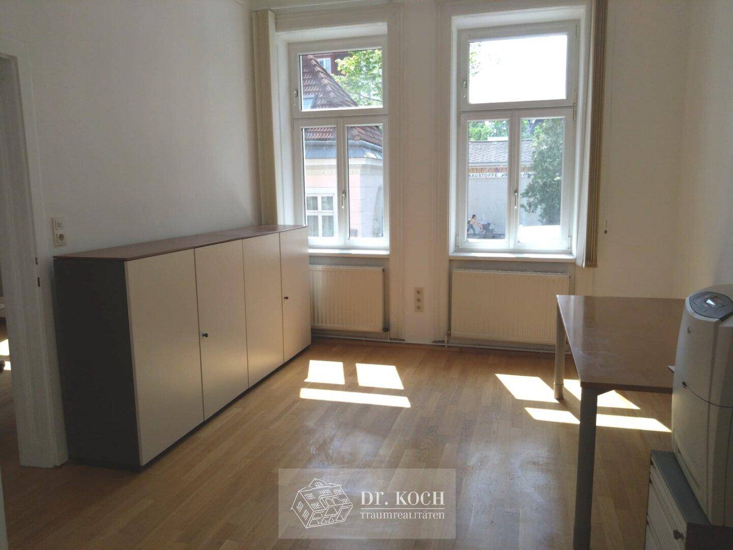 Helles Büro mit Holzboden, großen Fenstern und einem langen Schrank, bietet viel Stauraum und Tageslicht.