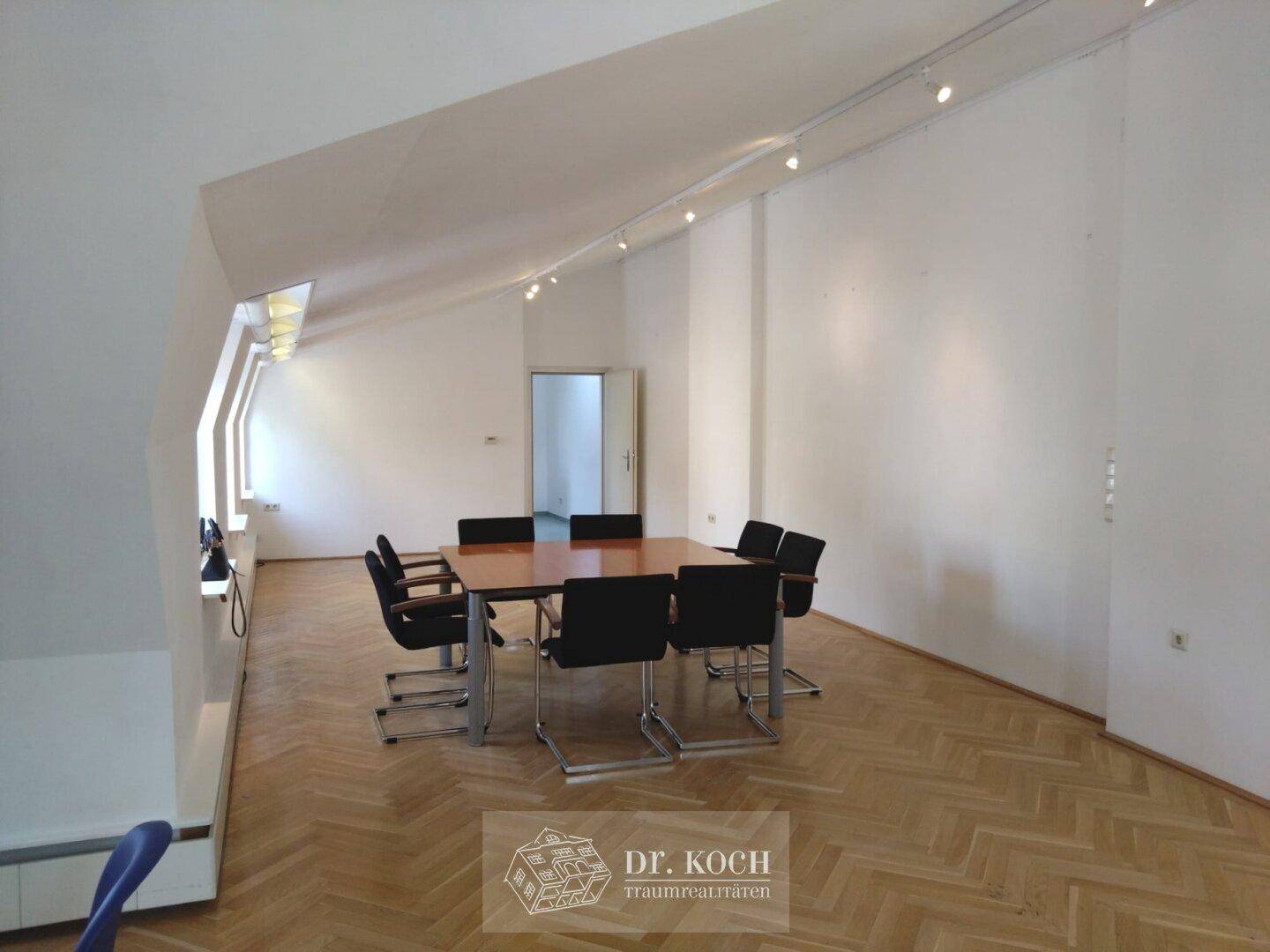 Geräumiger Dachgeschossraum mit Holzboden, Konferenztisch und schrägen Wänden, ideal für Besprechungen.