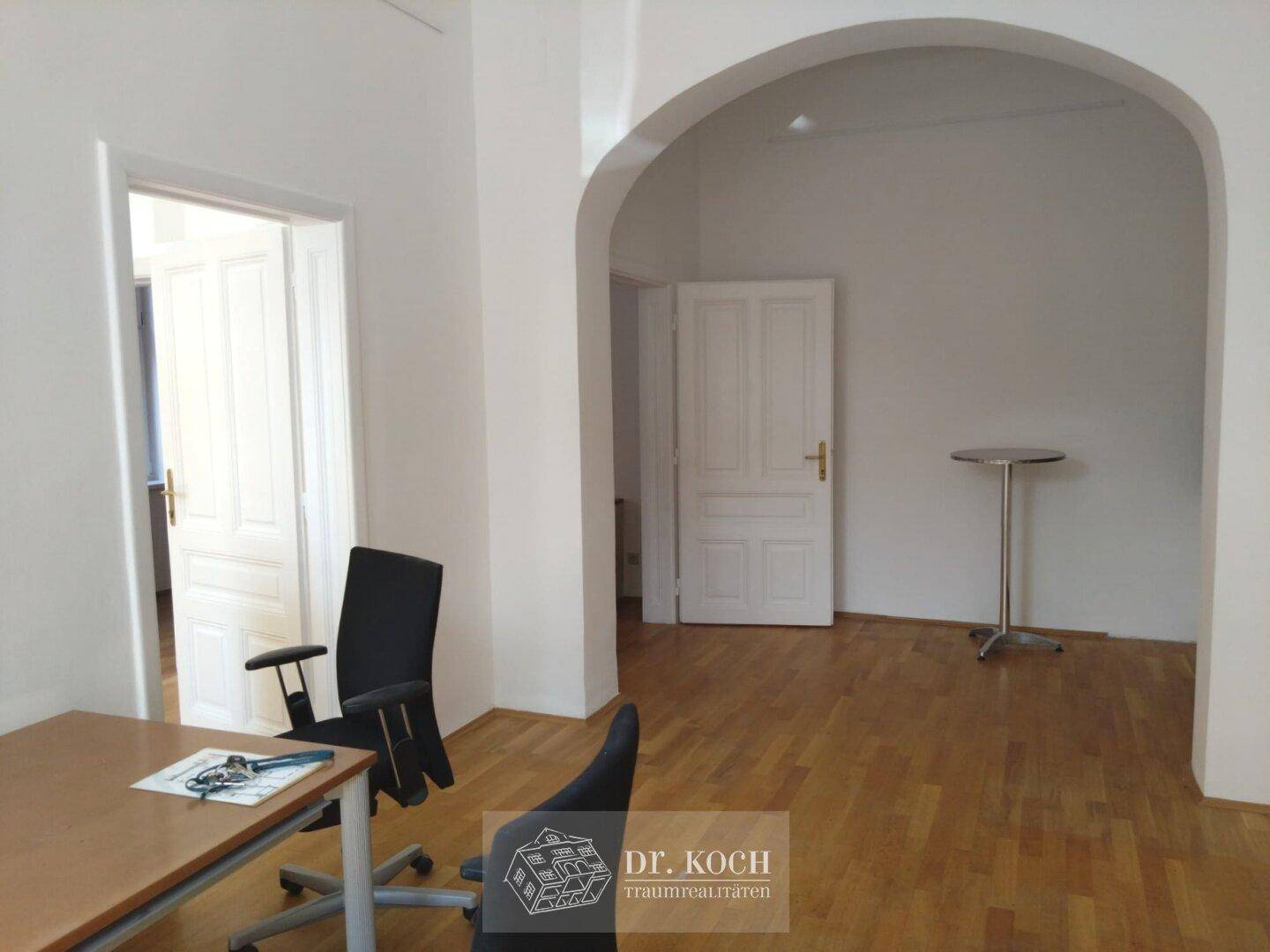 Geräumiges Büro mit Holzboden, einem eleganten Bogen und weißen Türen, bietet vielseitige Nutzungsmöglichkeiten.