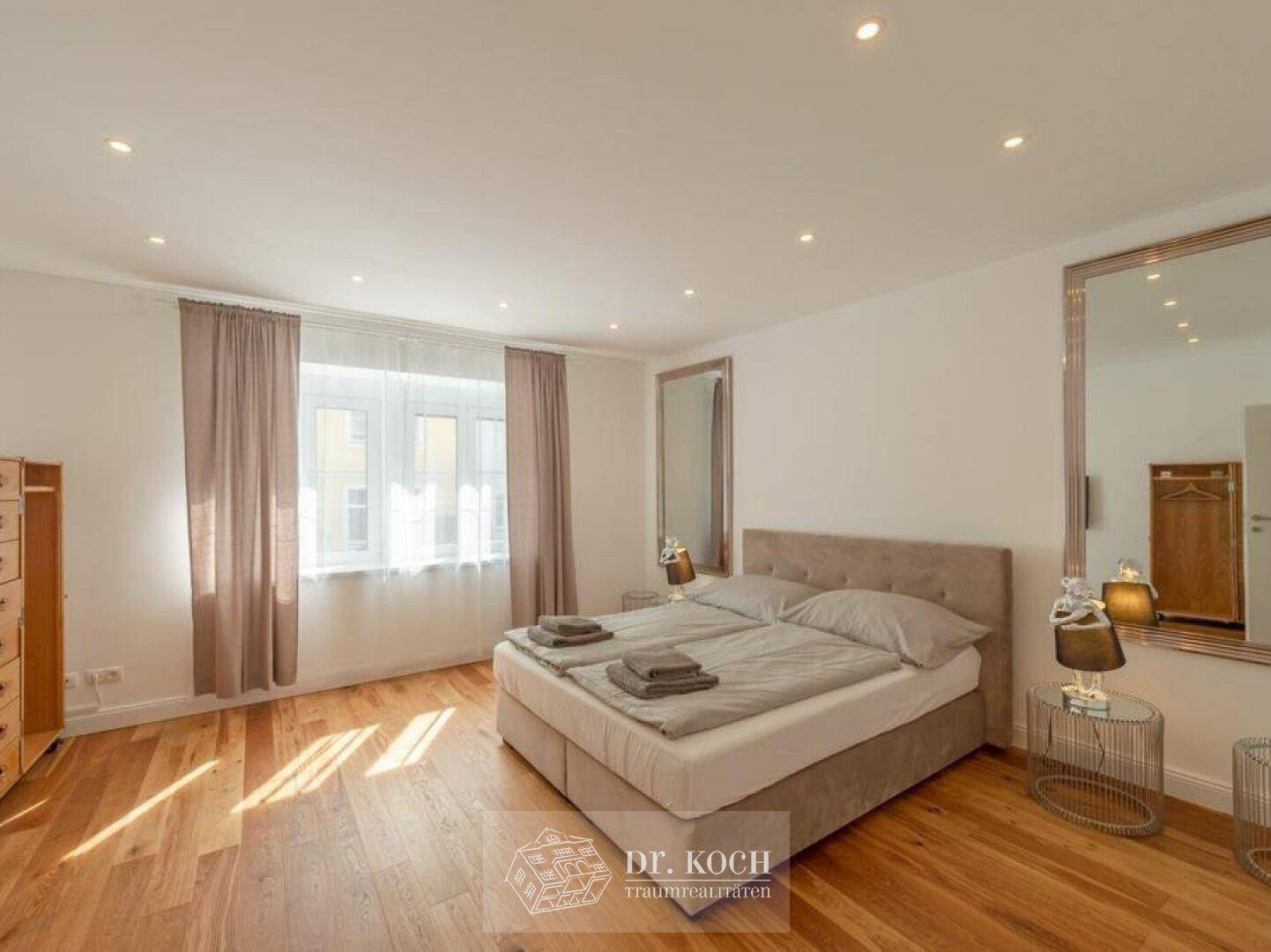 Helles Schlafzimmer mit Doppelbett, Holzboden und großem Spiegel.