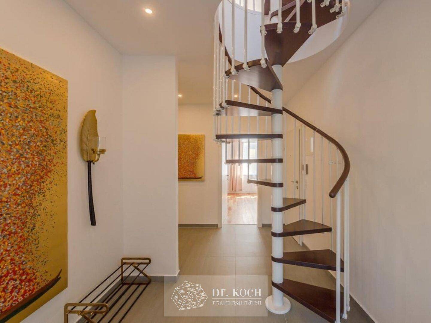 Heller Flur mit Wendeltreppe, Kunstwerken und modernem Bodenbelag.