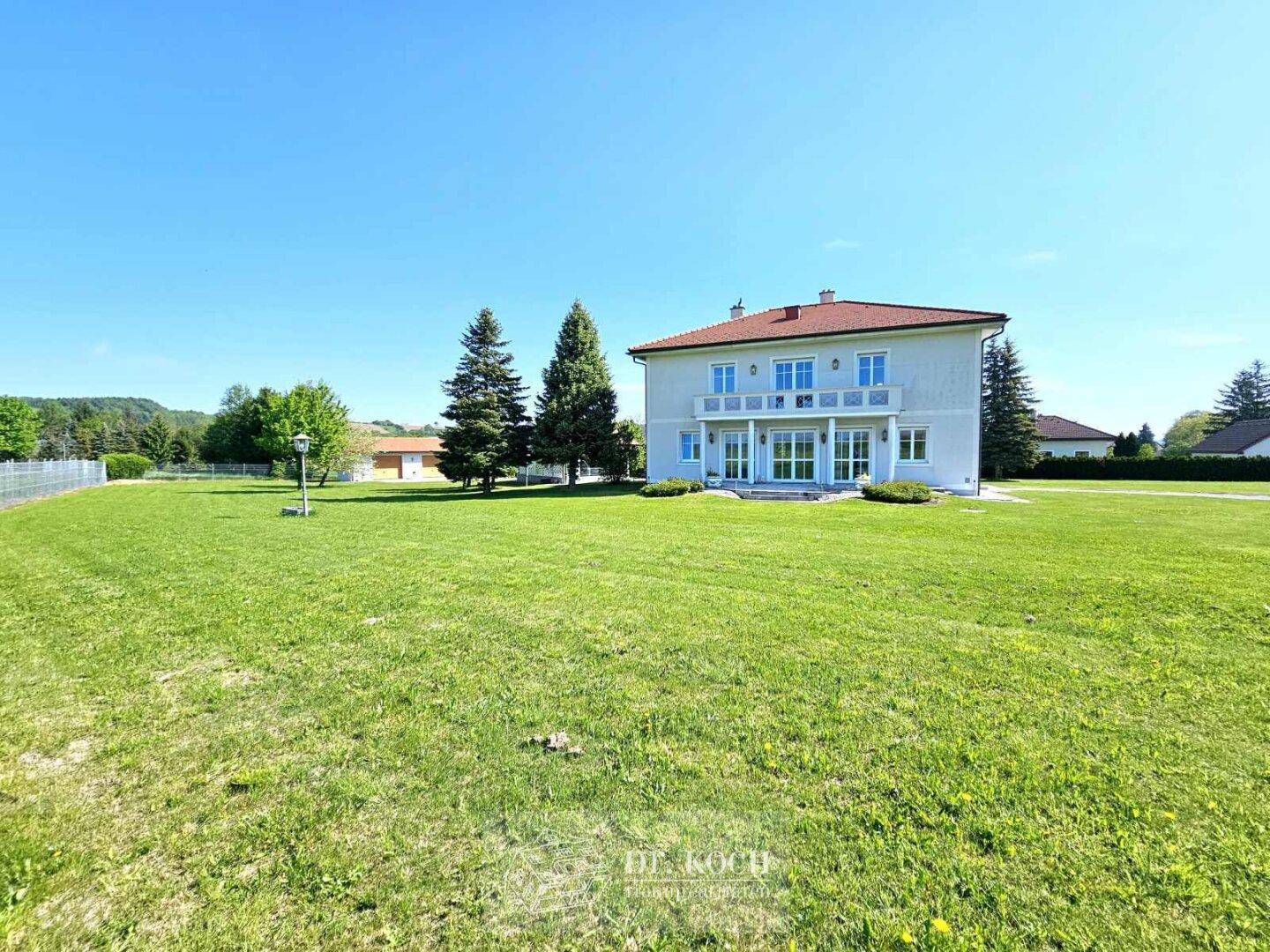 Rückansicht des Hauses mit großer Rasenfläche und Zugang zu den Terrassenbereichen im Grünen.