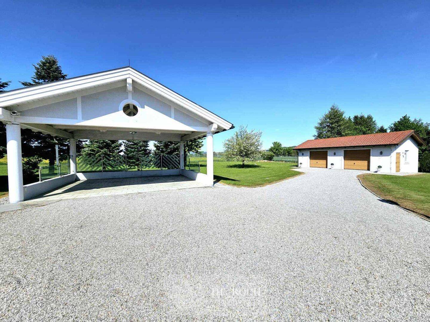 Geräumiger Carport und separate Doppelgarage mit Schotterauffahrt auf dem weitläufigen Grundstück.