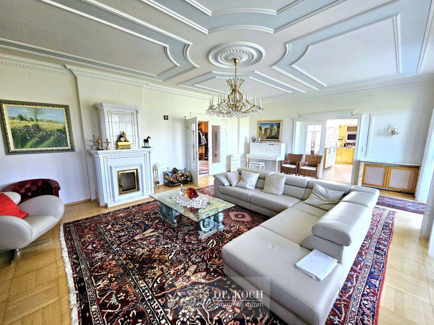 Großzügiges Wohnzimmer mit Stuckdecke, Kamin und elegantem Parkettboden, eingerichtet mit klassischen Möbeln.