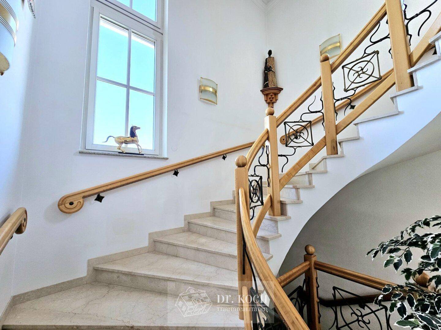 Elegante Treppe mit Marmorstufen und kunstvollem Holzgeländer, die die oberen Etagen verbindet.