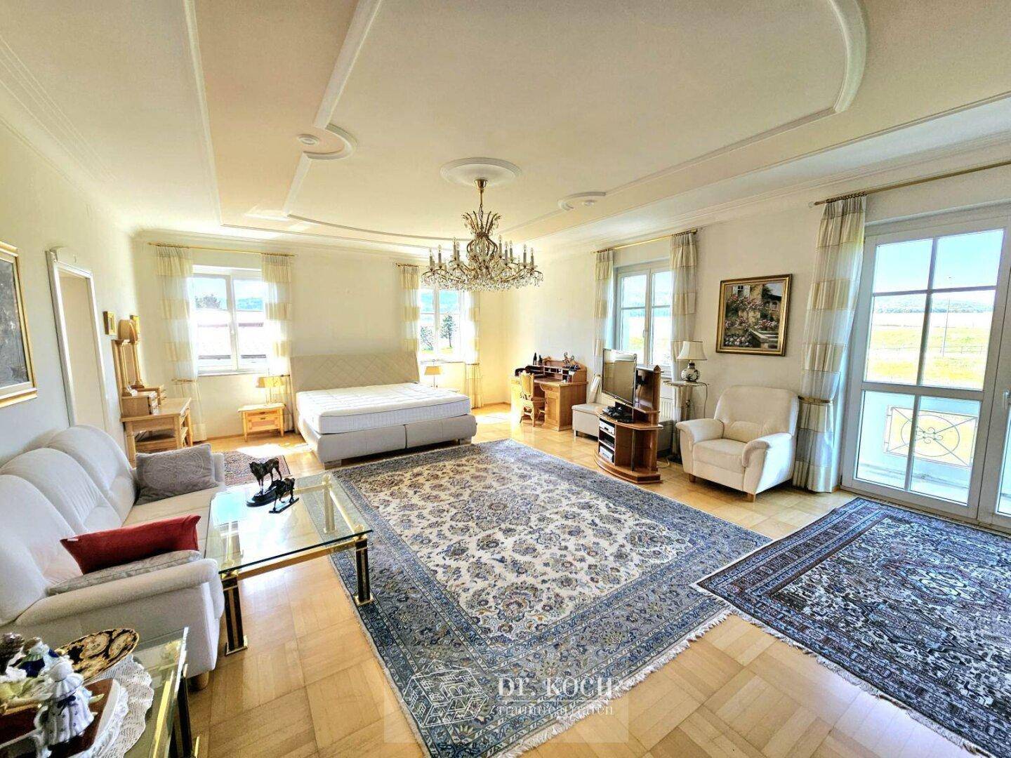 Großes Schlafzimmer mit Parkettboden, Stuckdecke und Zugang zum Balkon mit weitem Ausblick.