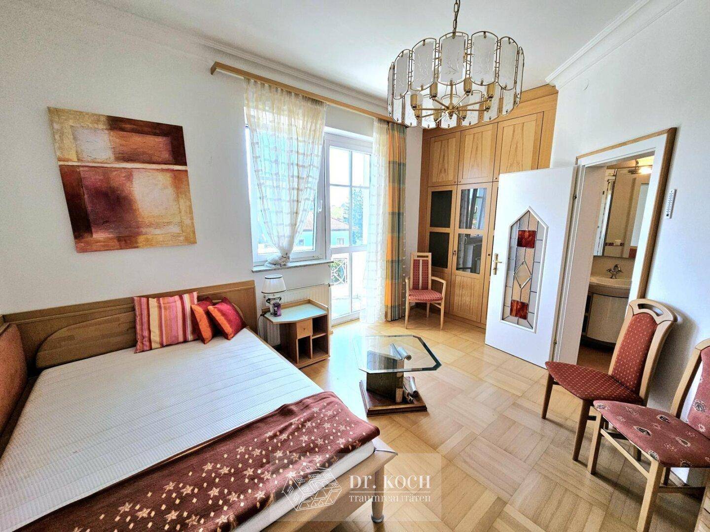 Helles Schlafzimmer mit Parkettboden, Holzschrank und Zugang zu einem französischen Balkon.