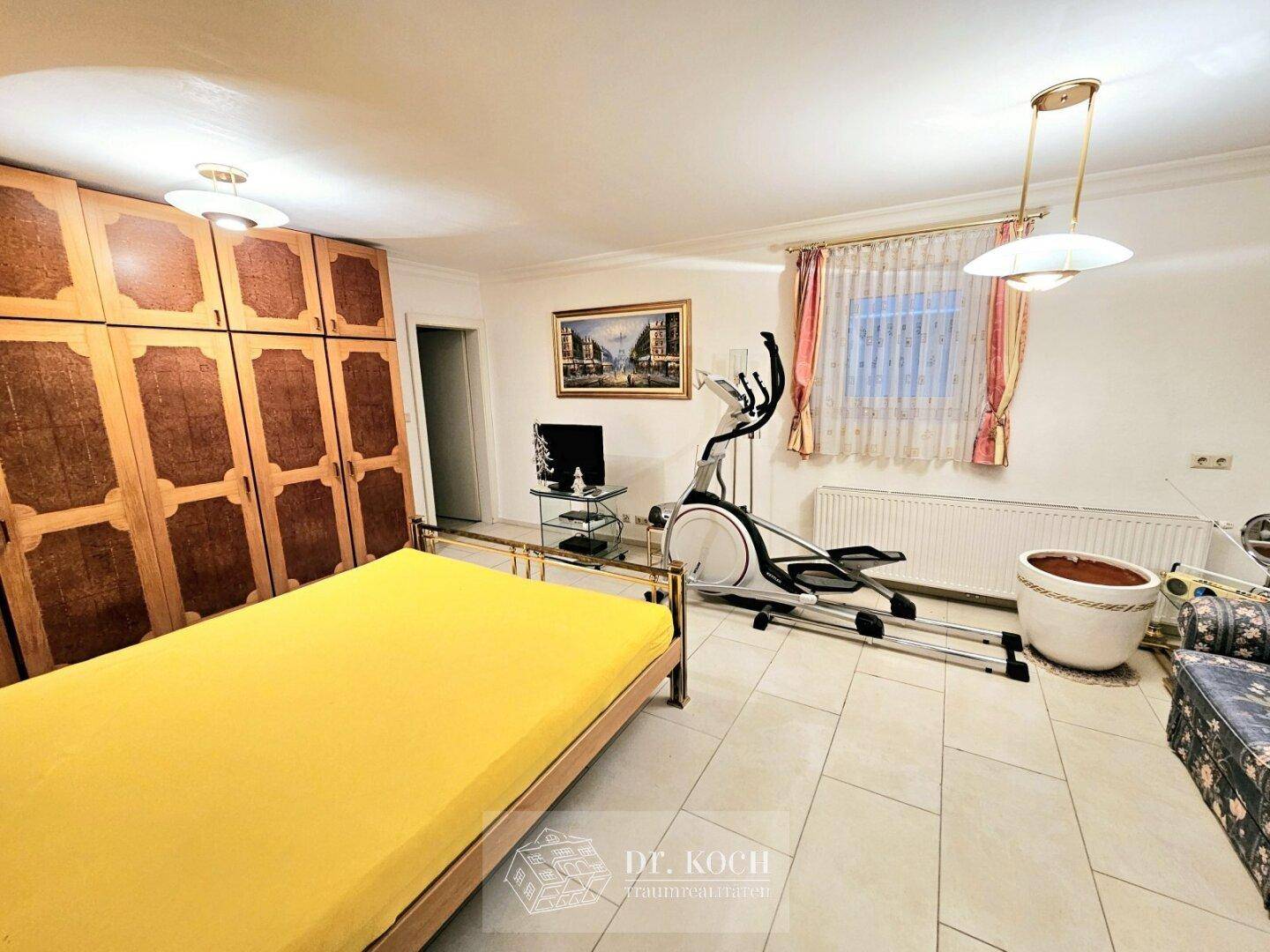 Geräumiges Schlafzimmer mit großem Kleiderschrank, Fliesenboden und Fitnessgerät.
