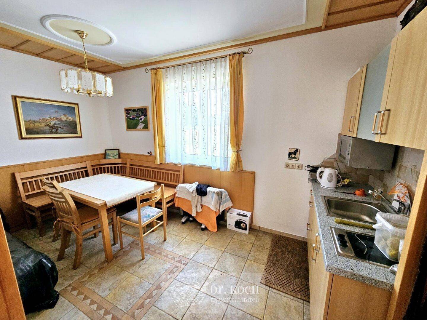 Gemütliche Wohnküche mit Essecke, Holzmöbeln und Fliesenboden.